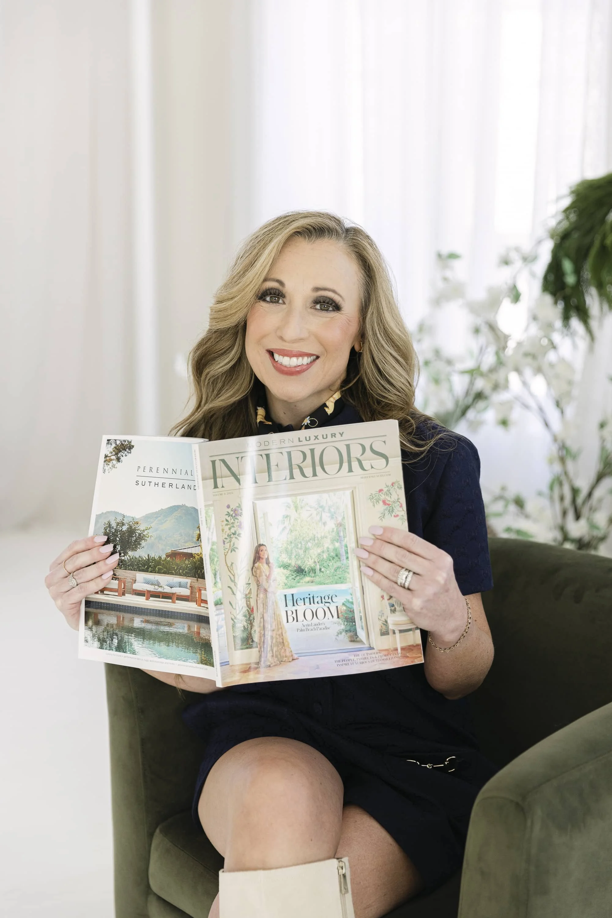 Xela Andrews, lead interior designer at Spaces in Bloom in Texas and Tennessee, smiling at the camera while holding a Modern Luxury Interiors magazine.