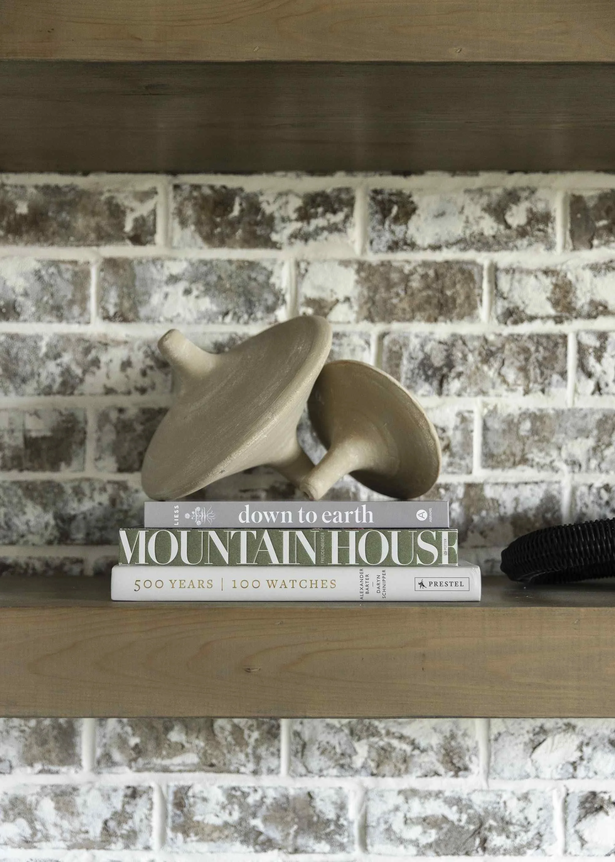 Interior decorating shelf styling tips with stacked coffee table books and clay mushroom sculptures on a rustic painted brick fireplace mantel.