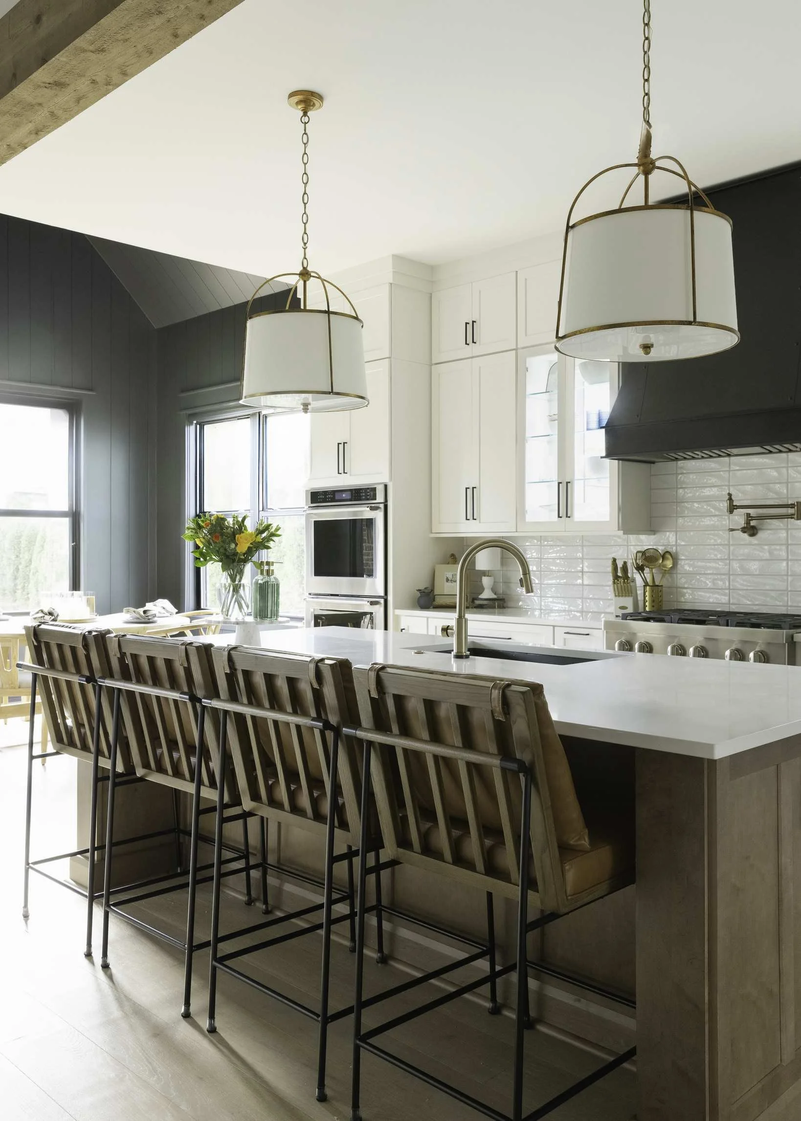 Light fixture upgrades with brass cage pendant lights over dark kitchen island, white shaker cabinets, and leather bar stools.