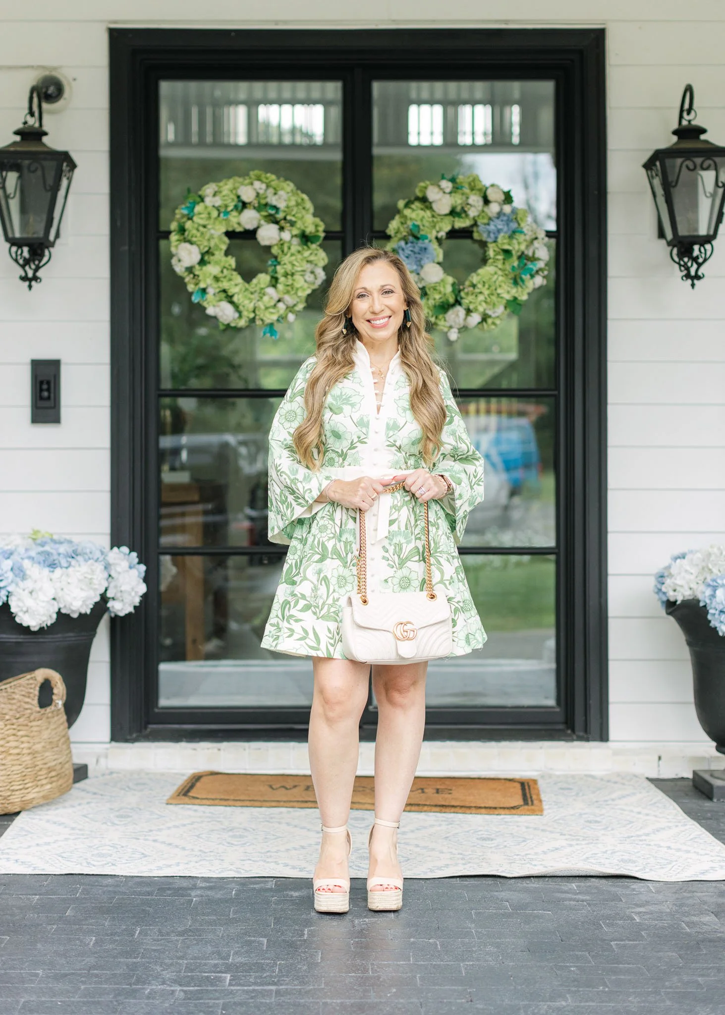 Welcoming entryway decor featuring black door, statement greenery wreath, and Nashville interior designer in floral dress