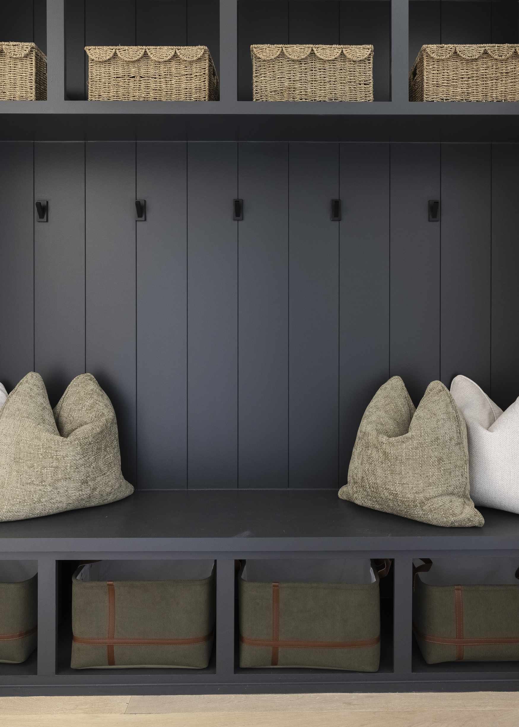 Organizing tips for mudroom with dark built-in bench, wall hooks, woven baskets on upper shelf, and canvas storage bins below.