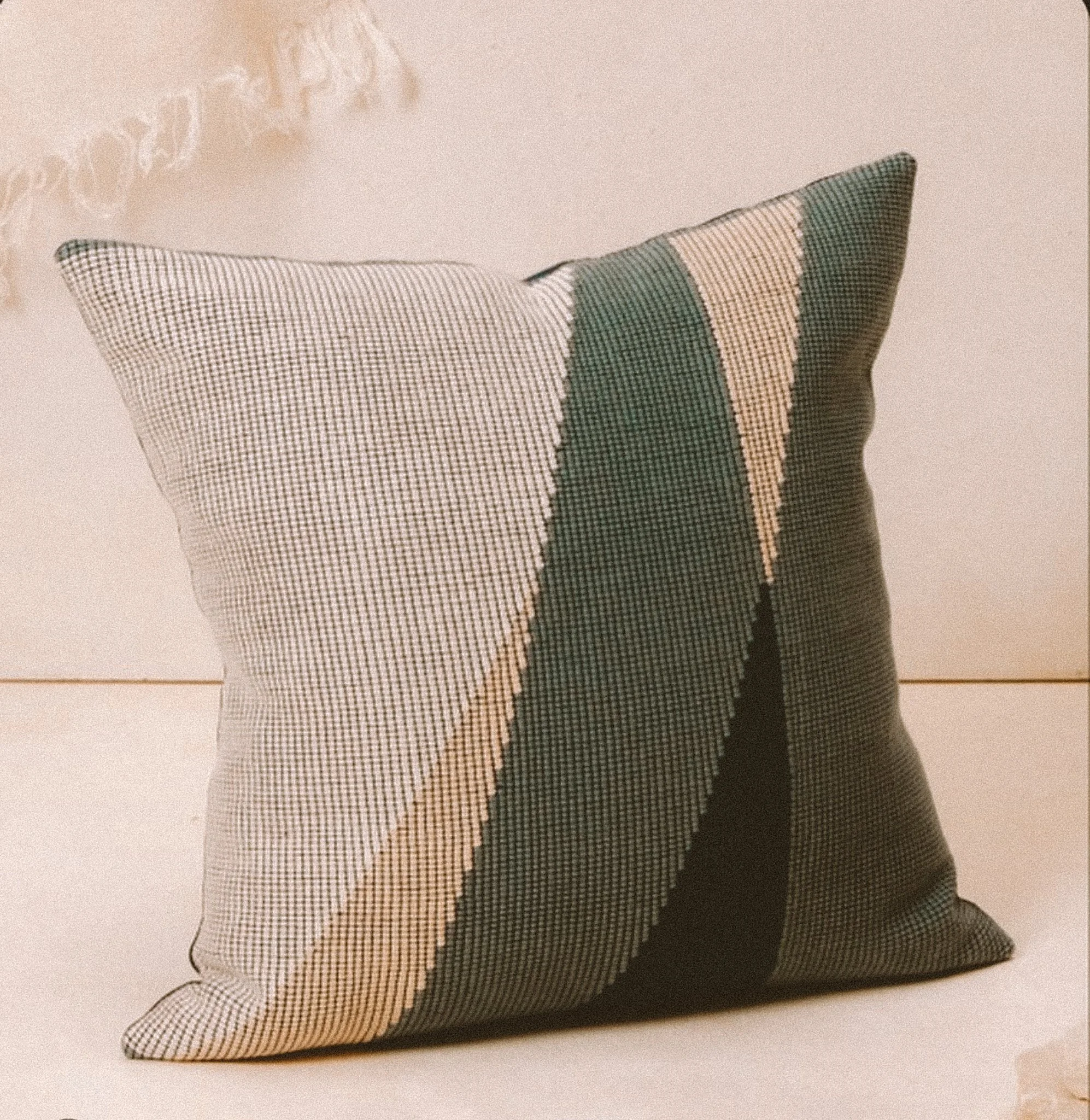 A decorative throw pillow with a geometric pattern of angled stripes in black, beige, and light gray, placed on a neutral background.