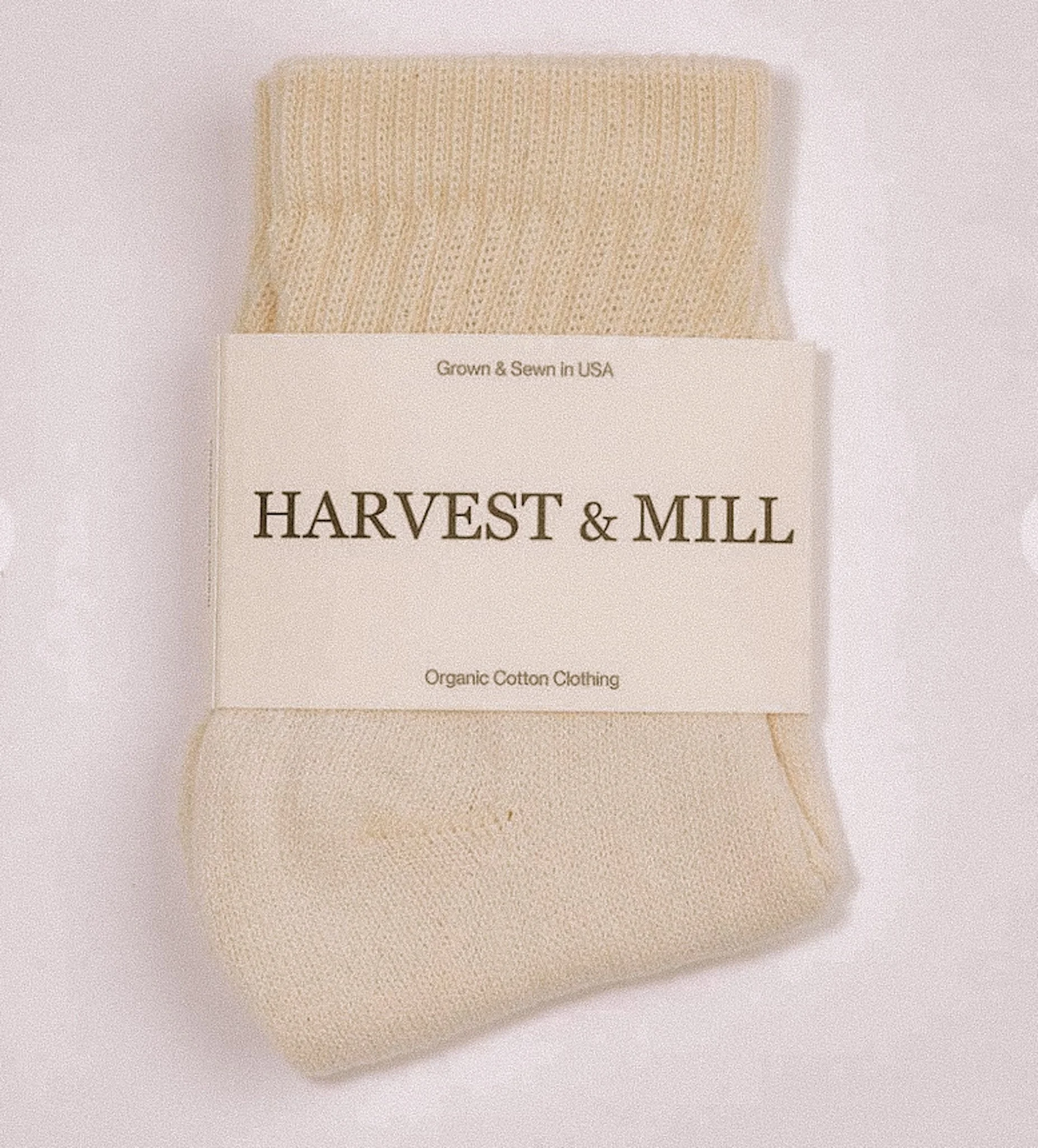 Beige organic cotton socks with a white label that reads 'Harvest & Mill', 'Grown & Sewn in USA', and 'Organic Cotton Clothing'.
