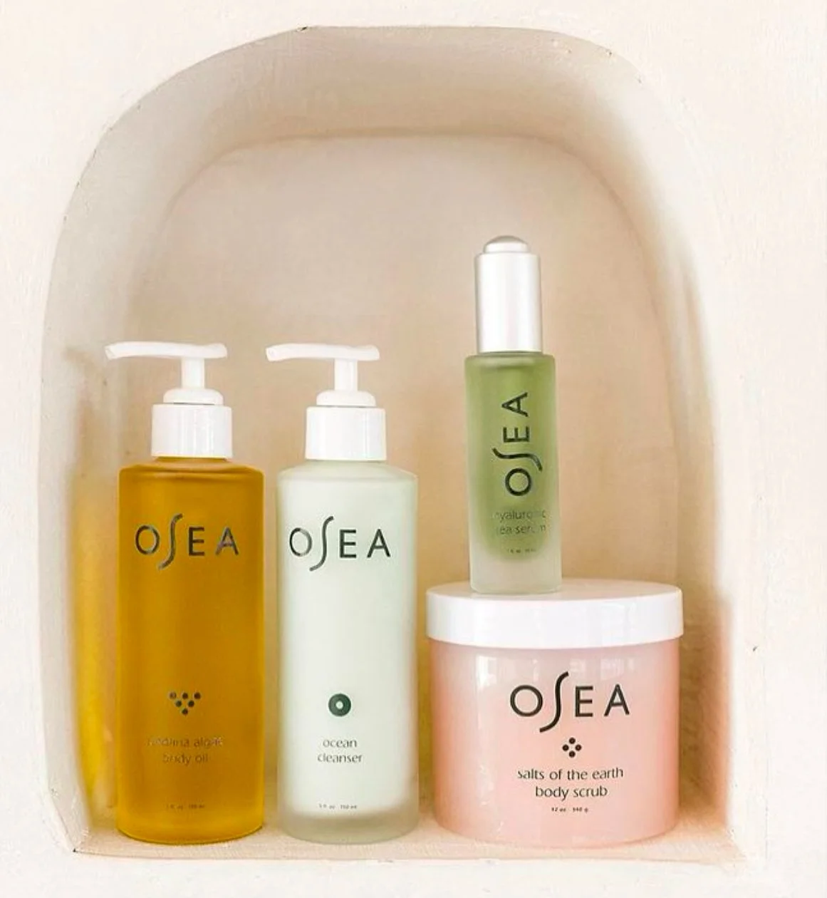 A collection of four OSEA skincare products displayed in a built-in wall nook, including body oil, cleanser, facial serum, and body scrub.