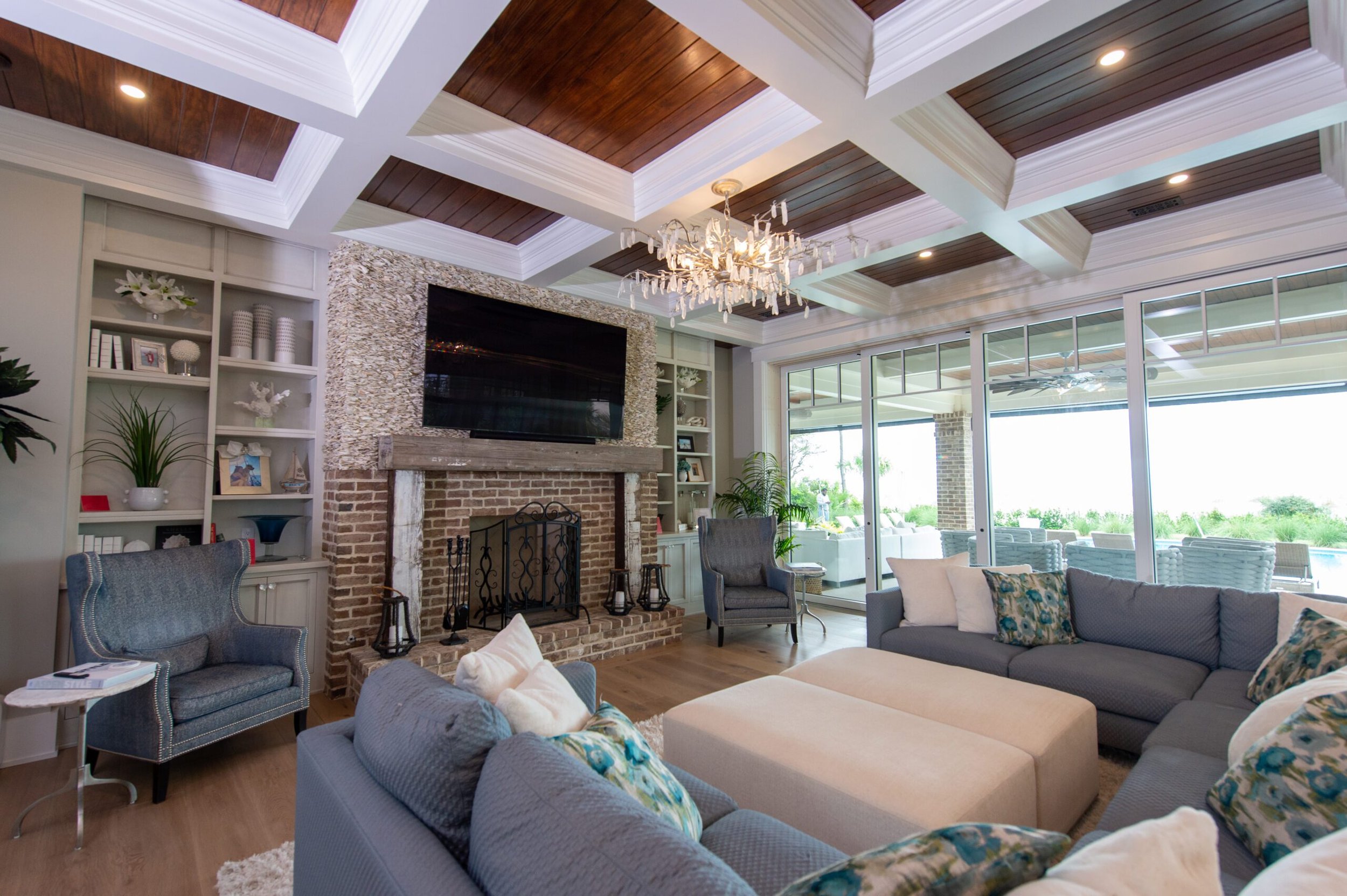 Luxurious living room with brick fireplace, TV, plush sofas, and large windows opening to a patio.