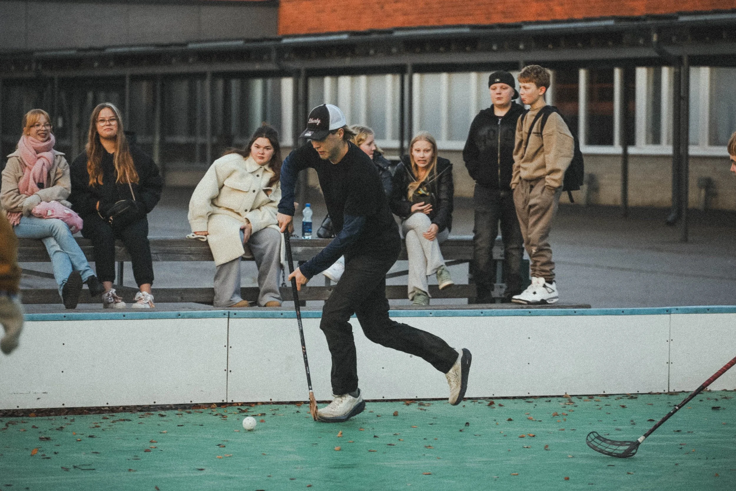 Henkilö pelaa salibandya ulkona, katsojat istuvat taustalla.