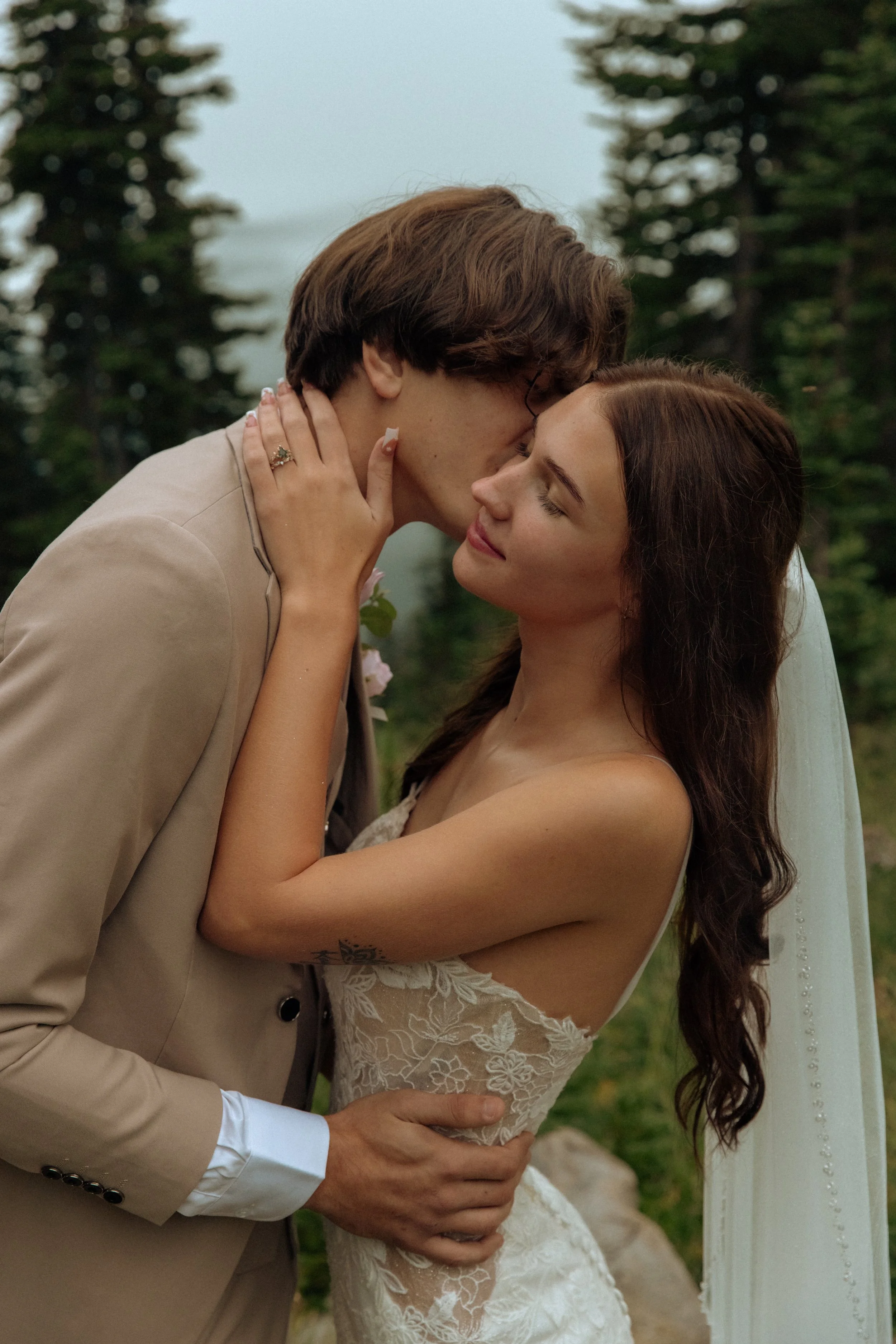 A bride and groom sharing a kiss outdoors with trees in the background.