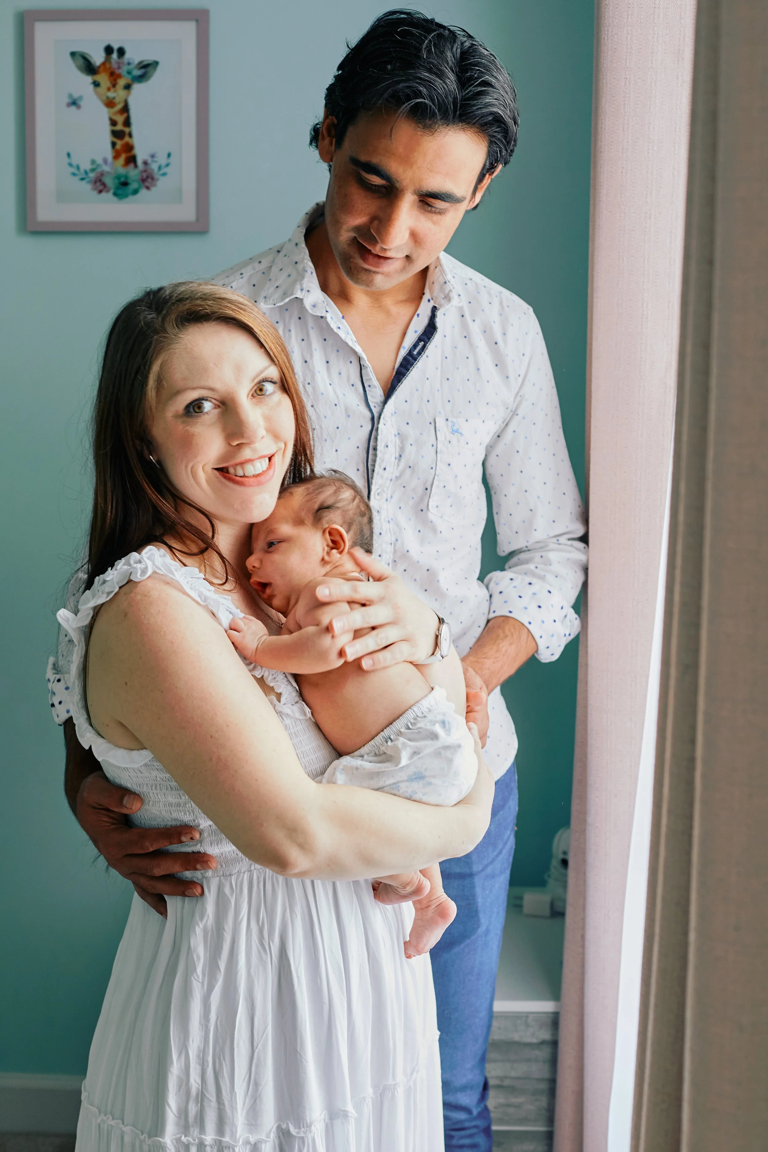Portrait of mom, dad and their baby standing in front of a window in the nursery
