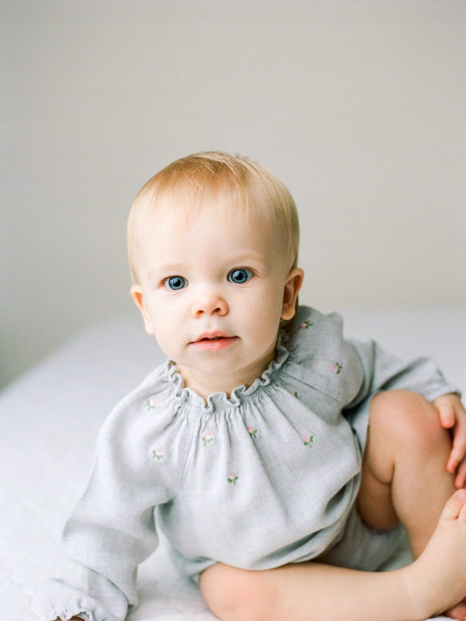 Young baby sitting on bed wearing grey shirt