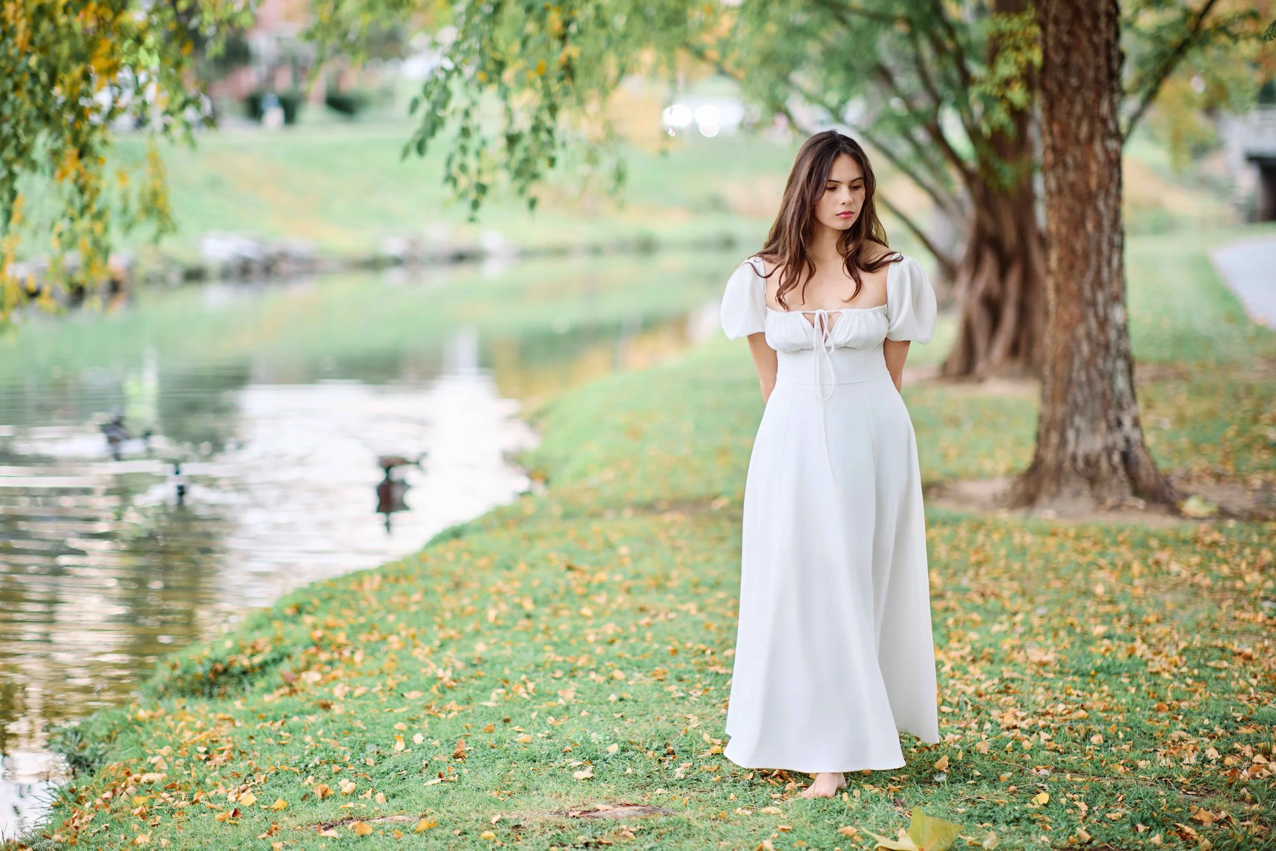 Senior portrait of a brunette girl wearing a white dress walking along side a river