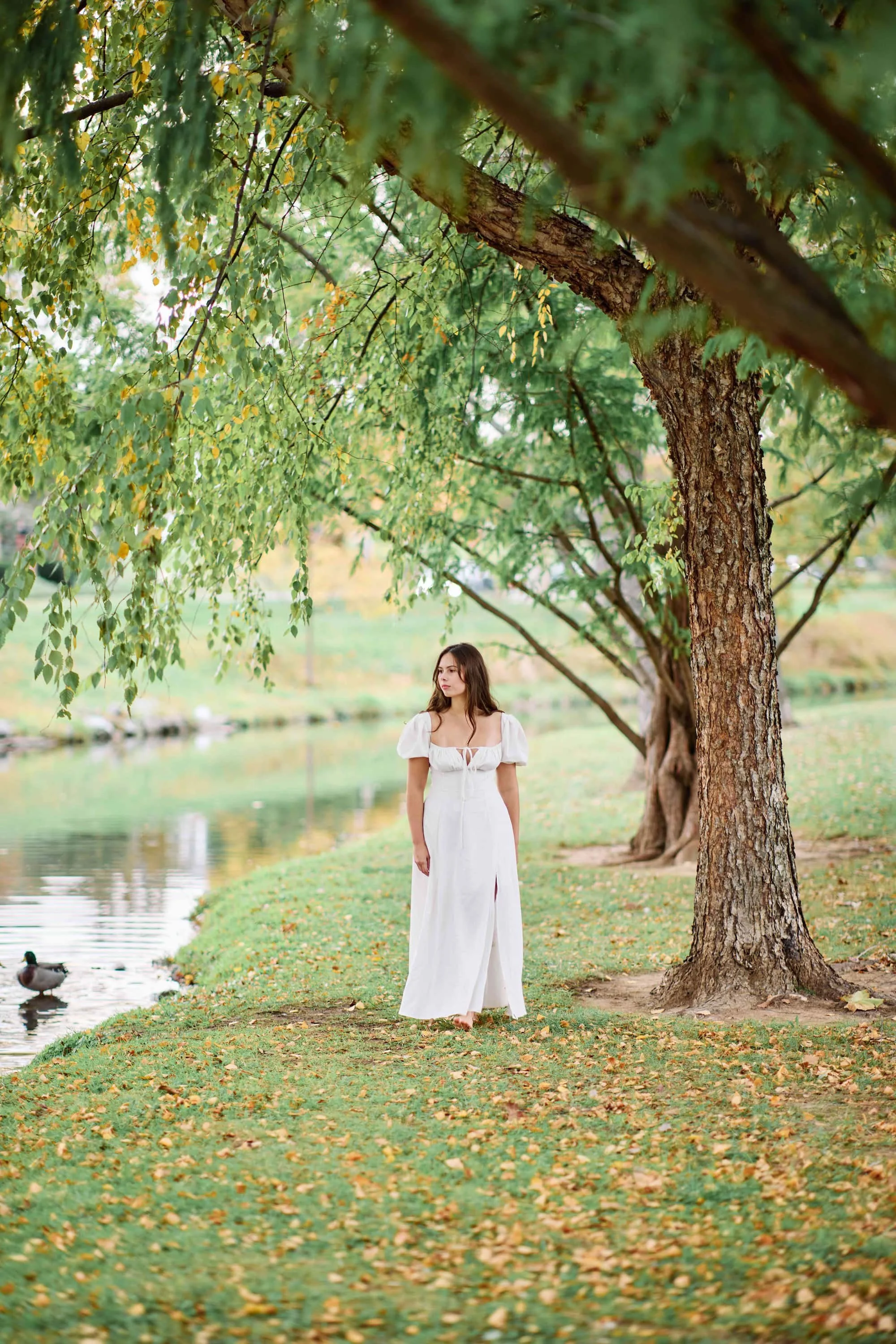 Senior portrait of a girl wearing a white dress walking along a river at Baker Park in Frederick MD