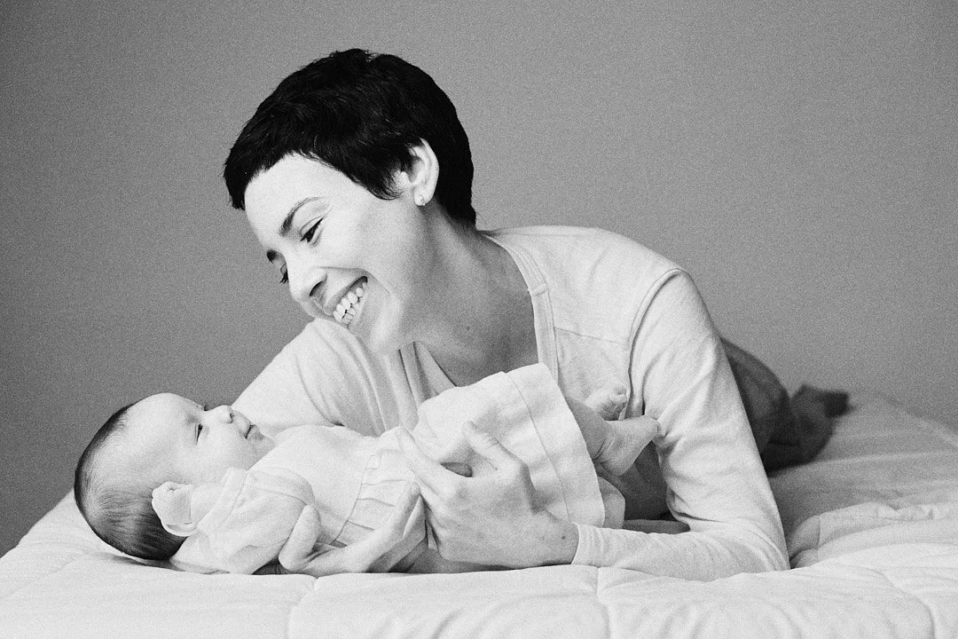 Black and white portrait of a new mom laying on a bed with her newborn baby girl