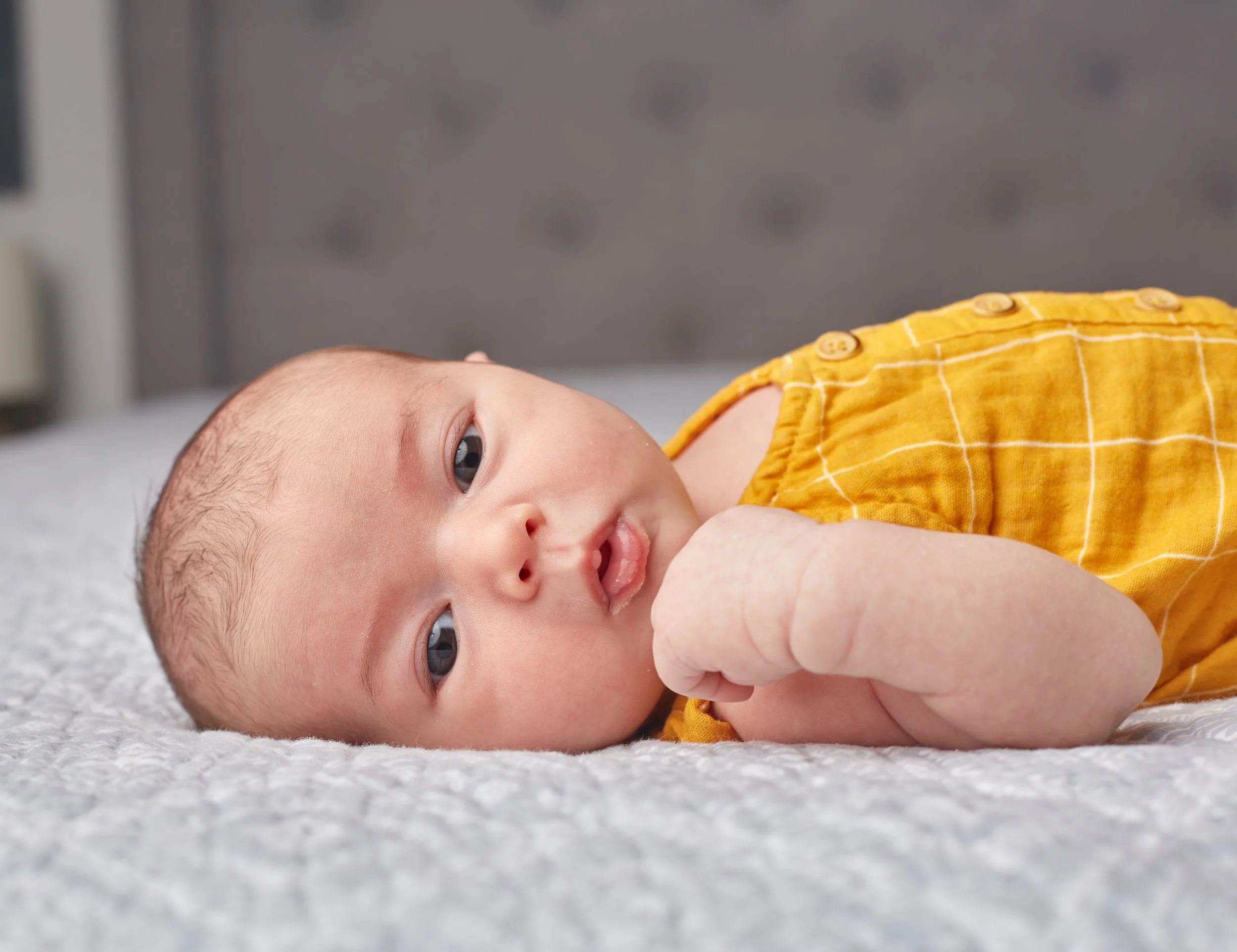 Newborn portrait of A baby lying on a bed wearing a yellow checkered outfit.
