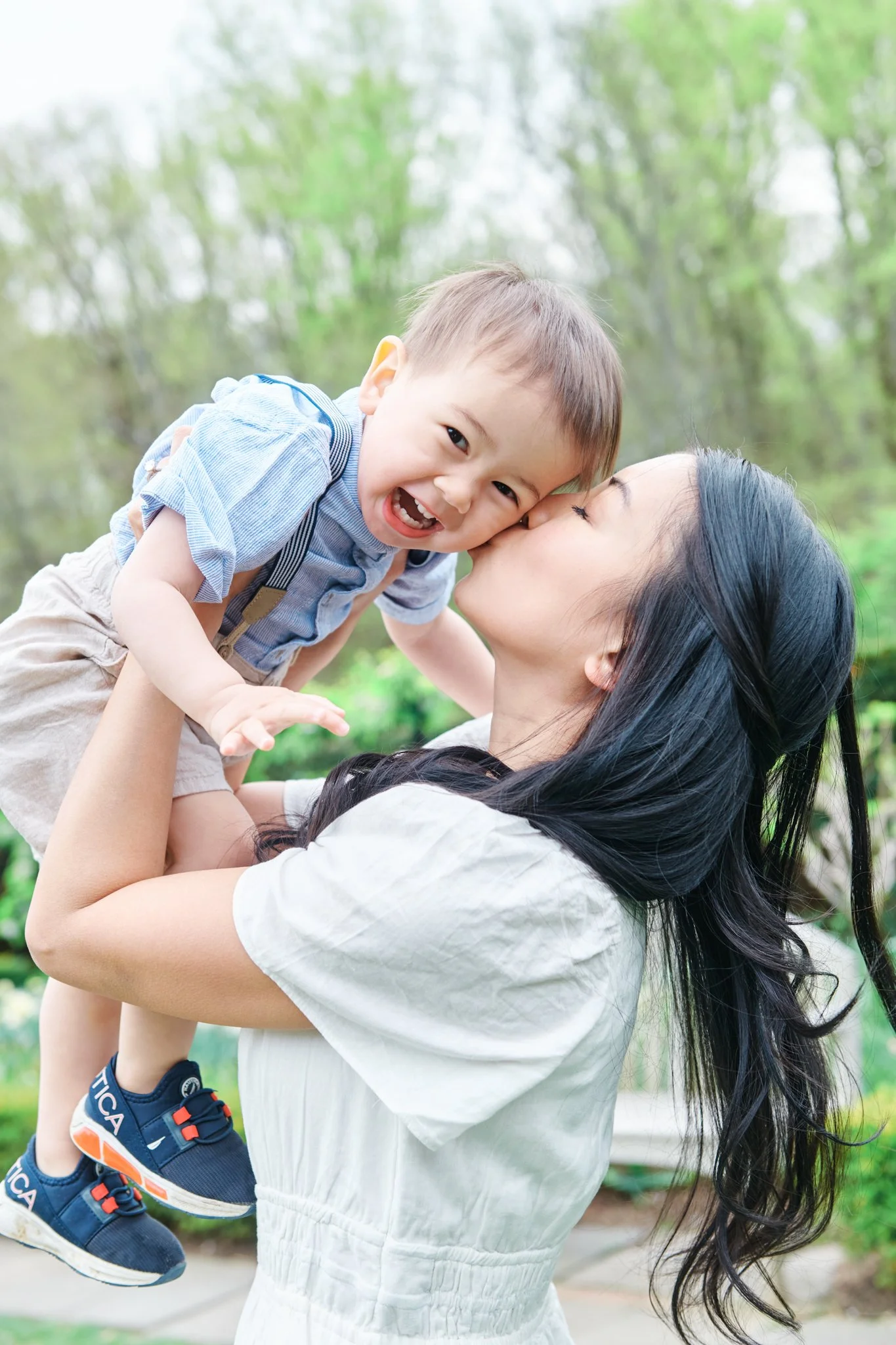 Mother kissing toddler boy outdoors, playful portrait