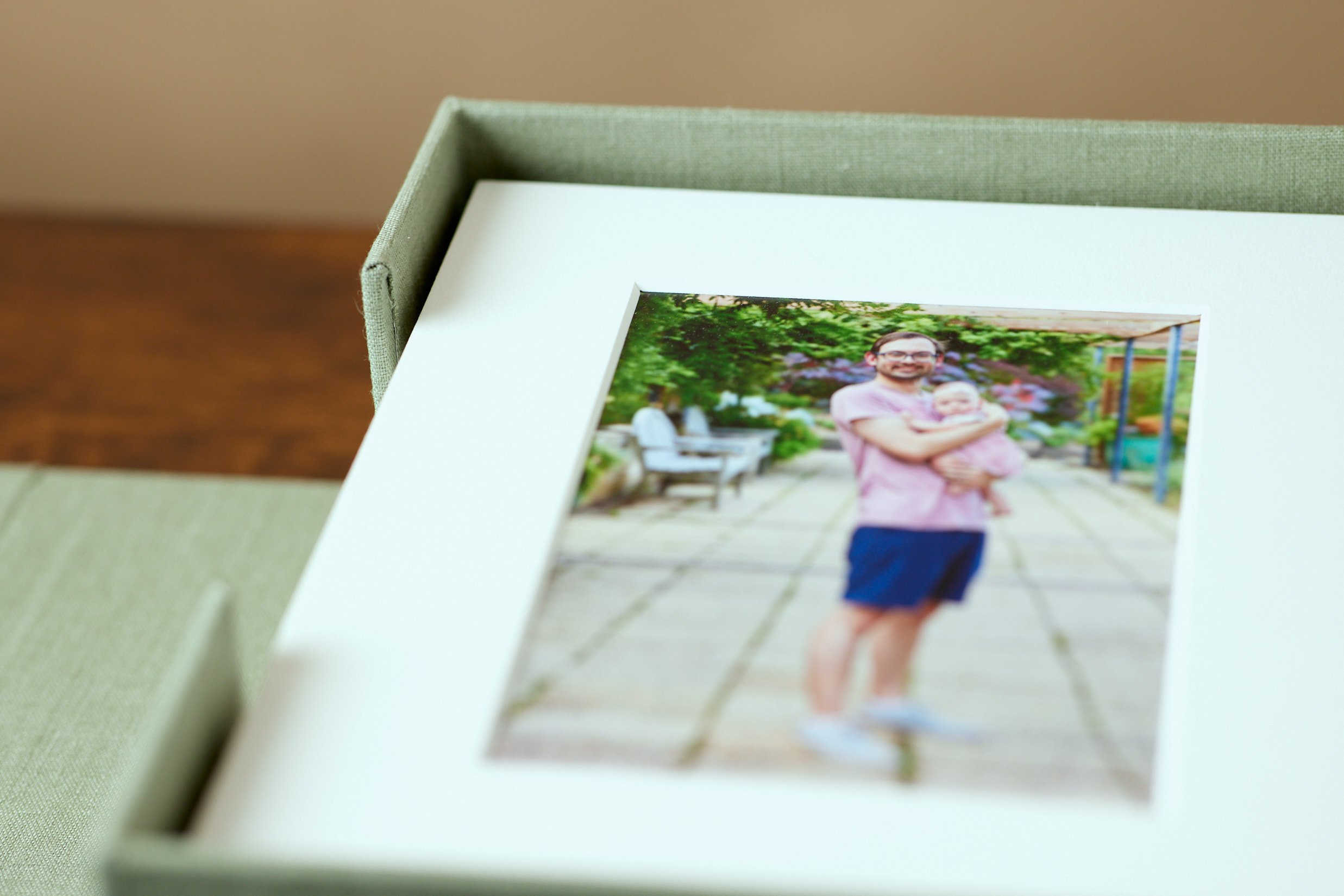 A framed photograph of a man holding a baby outdoors on a paved area, with greenery and benches in the background.