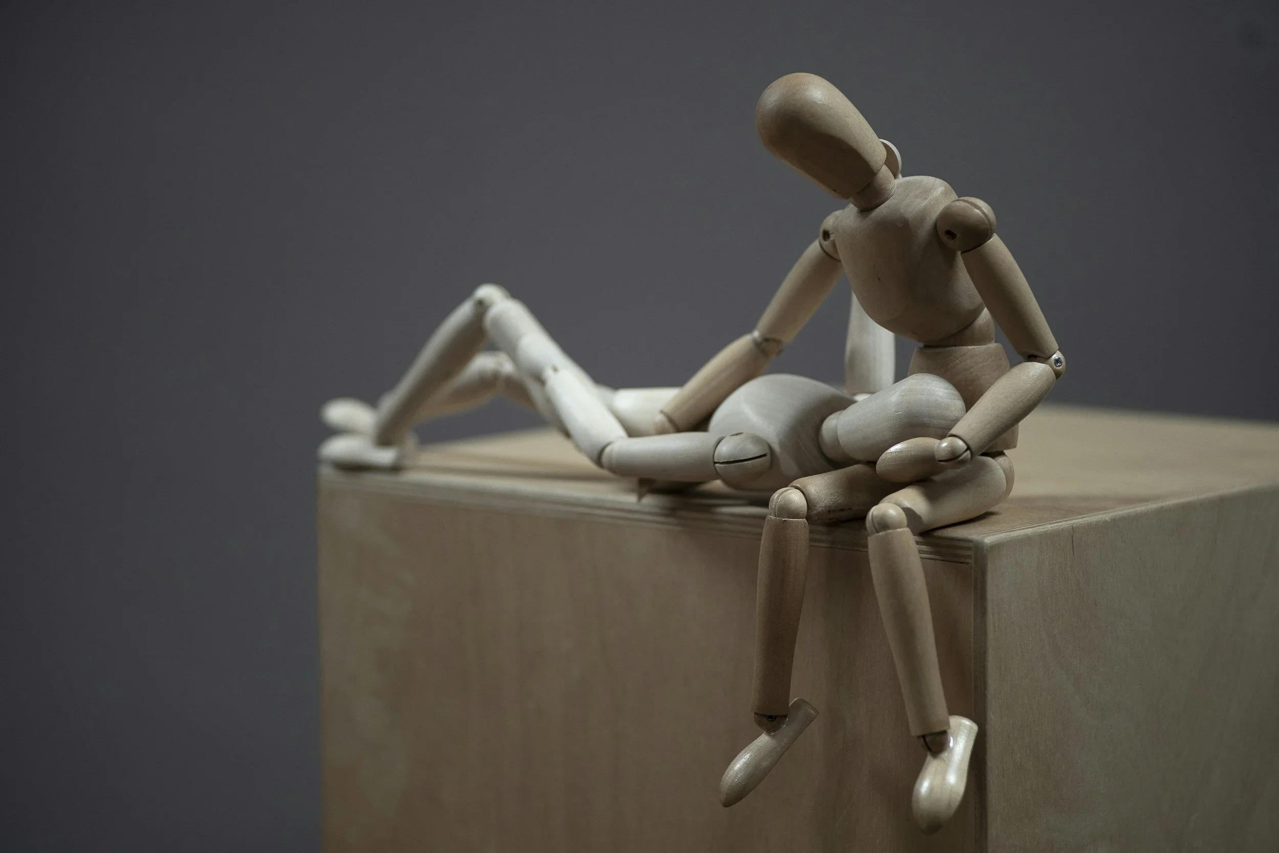 A wooden artist mannequin in a reclining pose on a wooden surface.