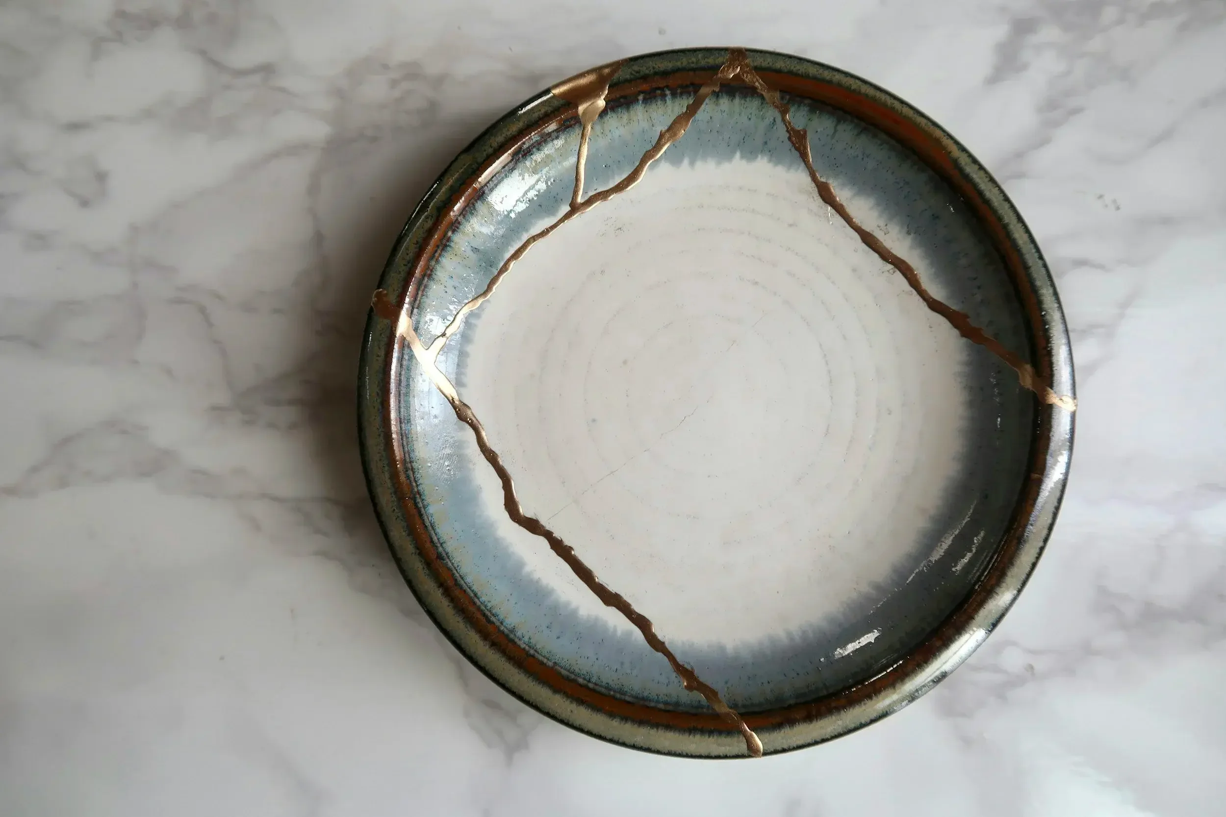 A ceramic bowl with a crackled glaze and gold accents, placed on a white marble surface.