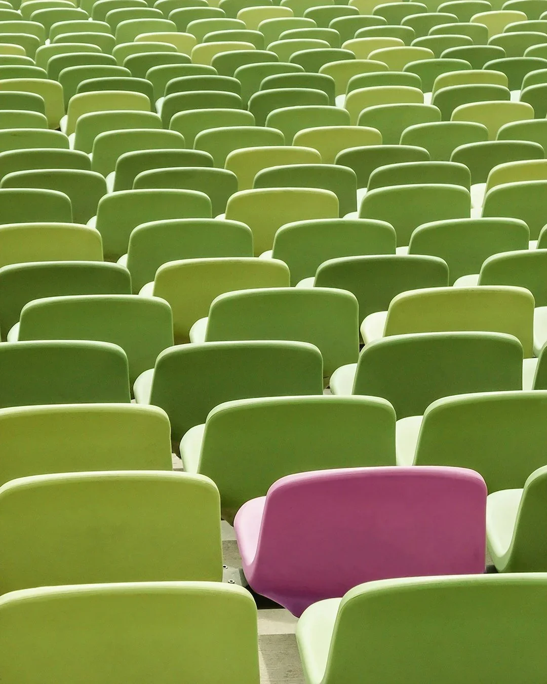 A large array of green chairs in an auditorium or conference hall, with a single purple chair among them.