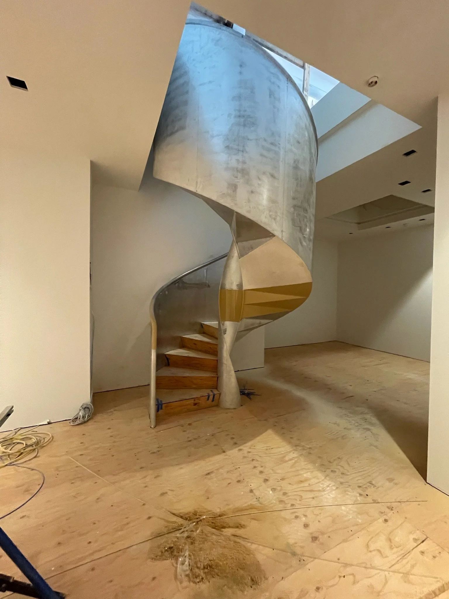 Unfinished modern spiral staircase with metal railing and wooden steps inside a building under construction.