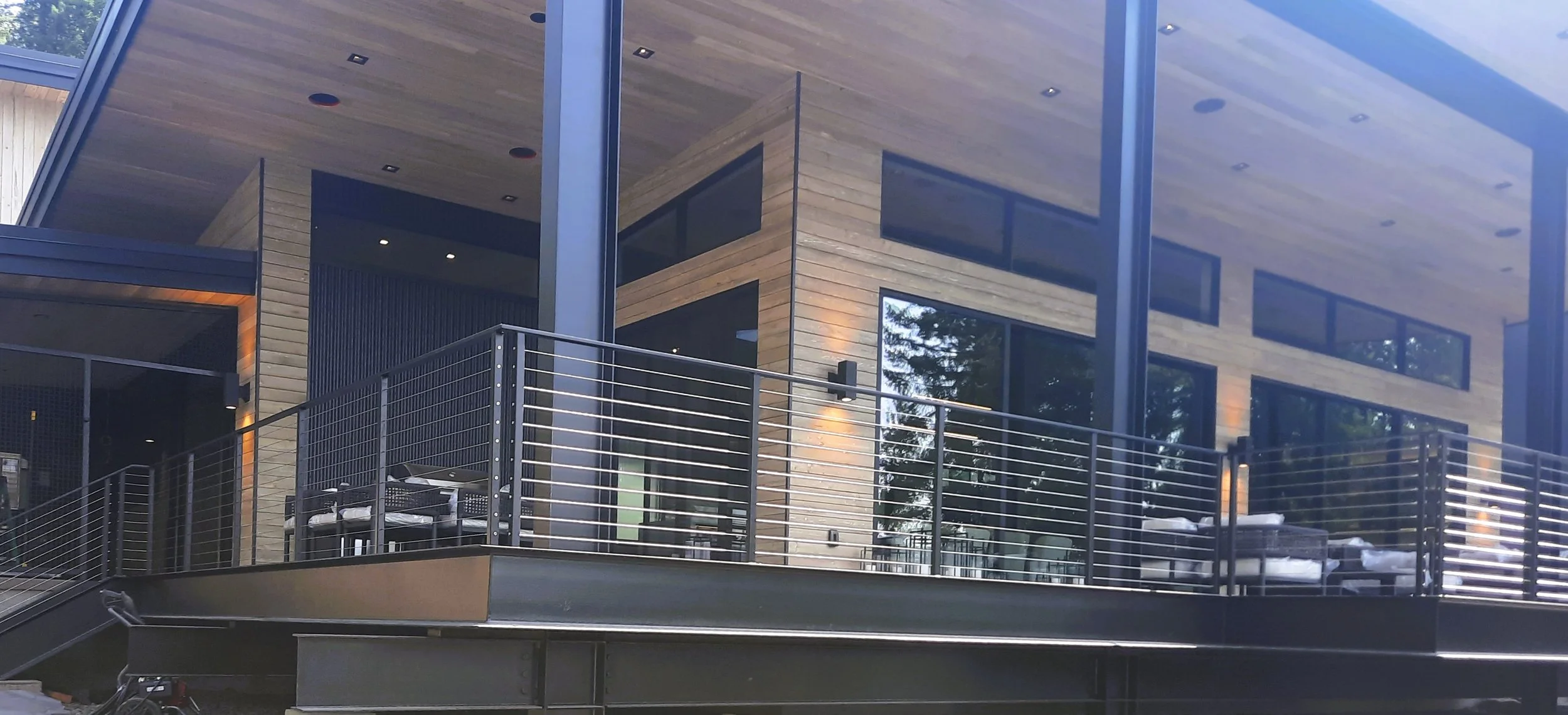 Modern house with large windows, wood siding, and a balcony with black metal railing.