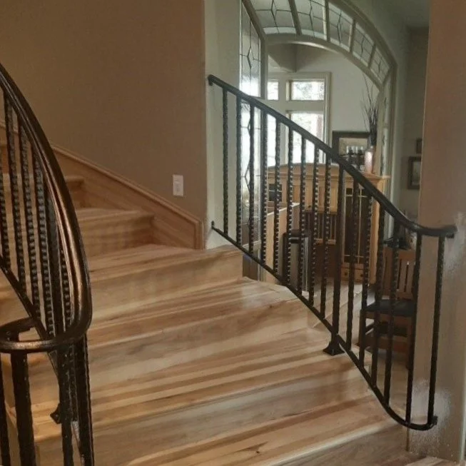Wooden staircase with a black metal railing leading to a second floor in a well-lit home interior.