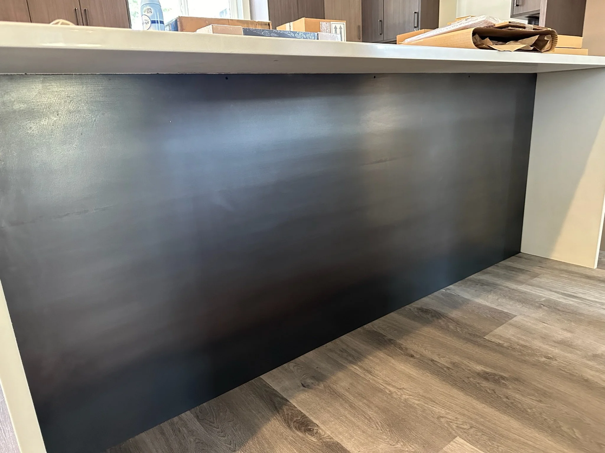 Close-up of a white kitchen island with a dark gray or black panel on the side, situated on a wooden floor, with a countertop on top and some items on it.