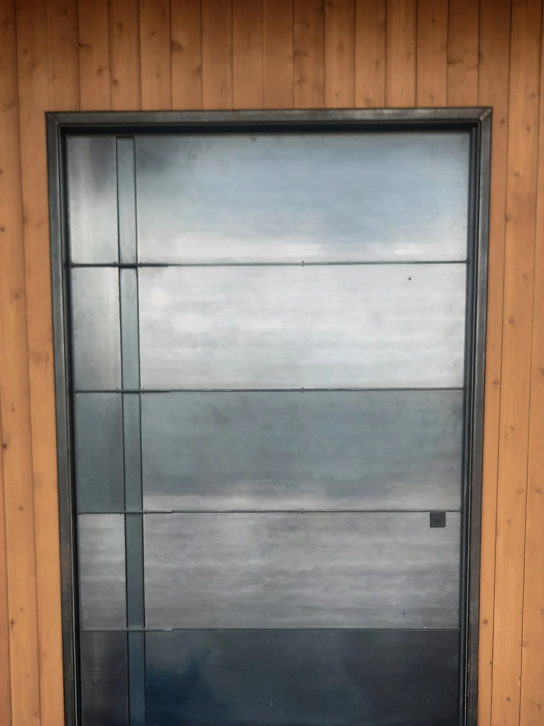 A modern, metallic garage door with horizontal panels, framed by wood-paneled wall.