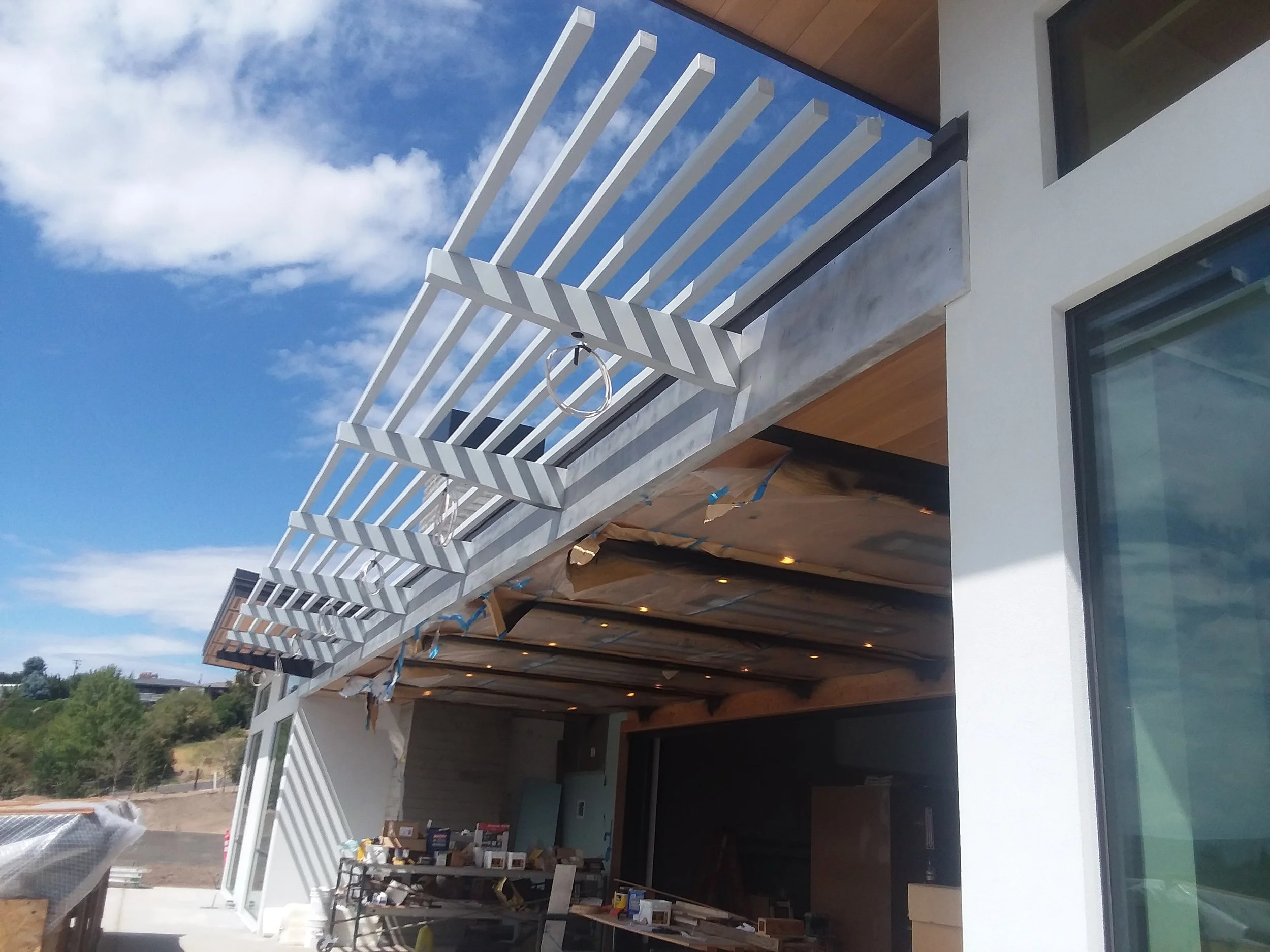 Under construction modern house with white horizontal slatted awnings on a sunny day.
