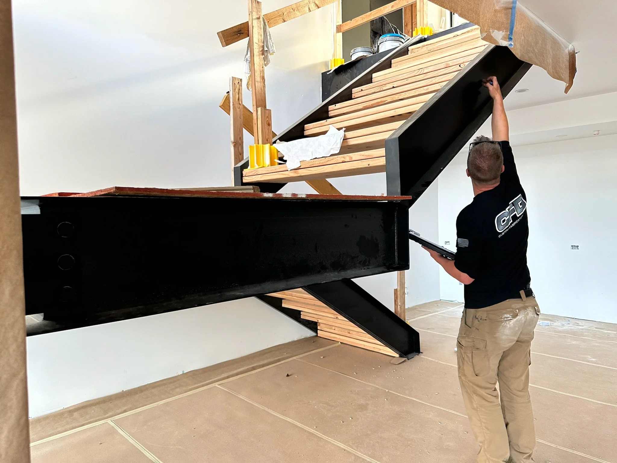 A man in professional attire is inspecting the framework of a modern staircase in a house under construction, with the staircase structure in progress.