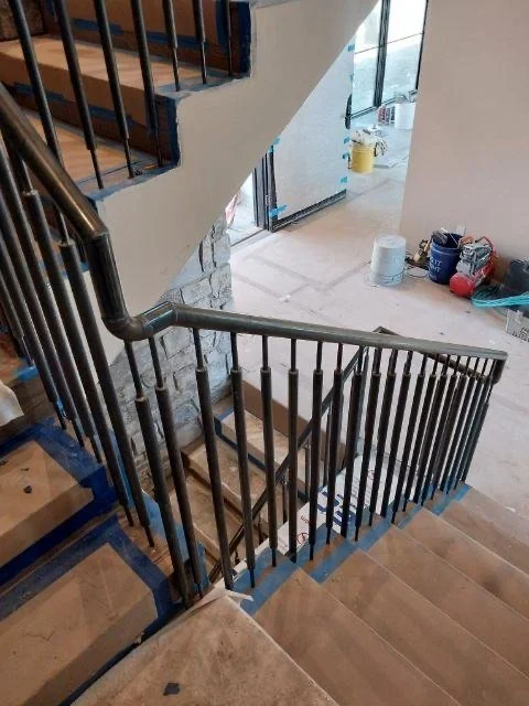 Indoor staircase with black metal railings and wooden steps, under construction with tools and supplies nearby.