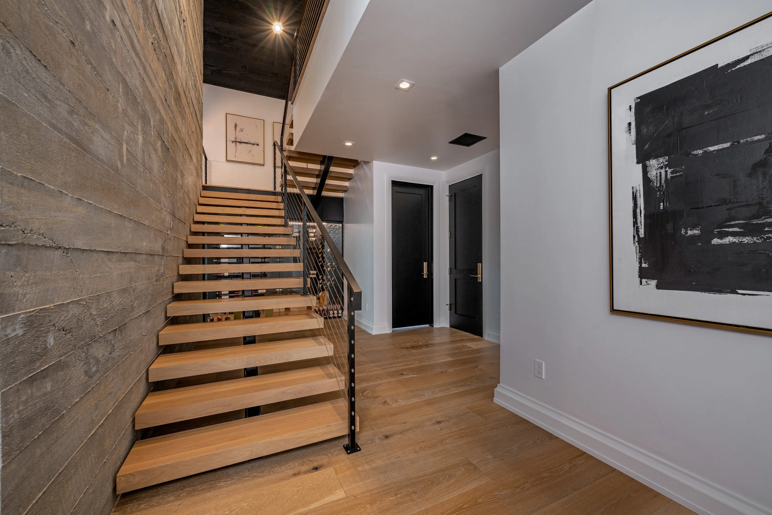 Interior of a modern house entryway with a wooden staircase, black doors, and abstract black and white artwork.