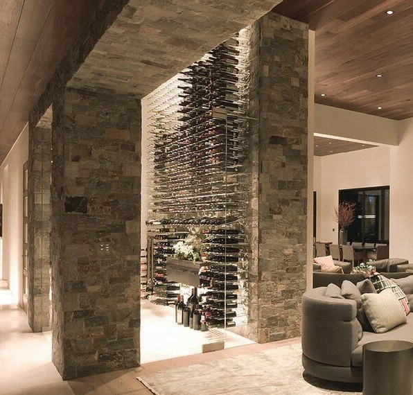Modern living room with a large wine cellar surrounded by stone walls and wooden ceilings.