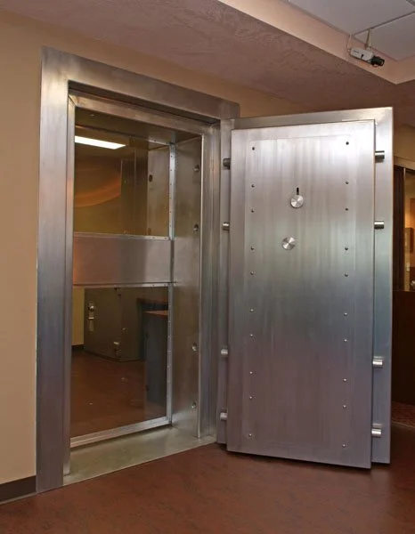 A large, heavy-duty metal safe door slightly ajar, revealing a secure vault environment inside.