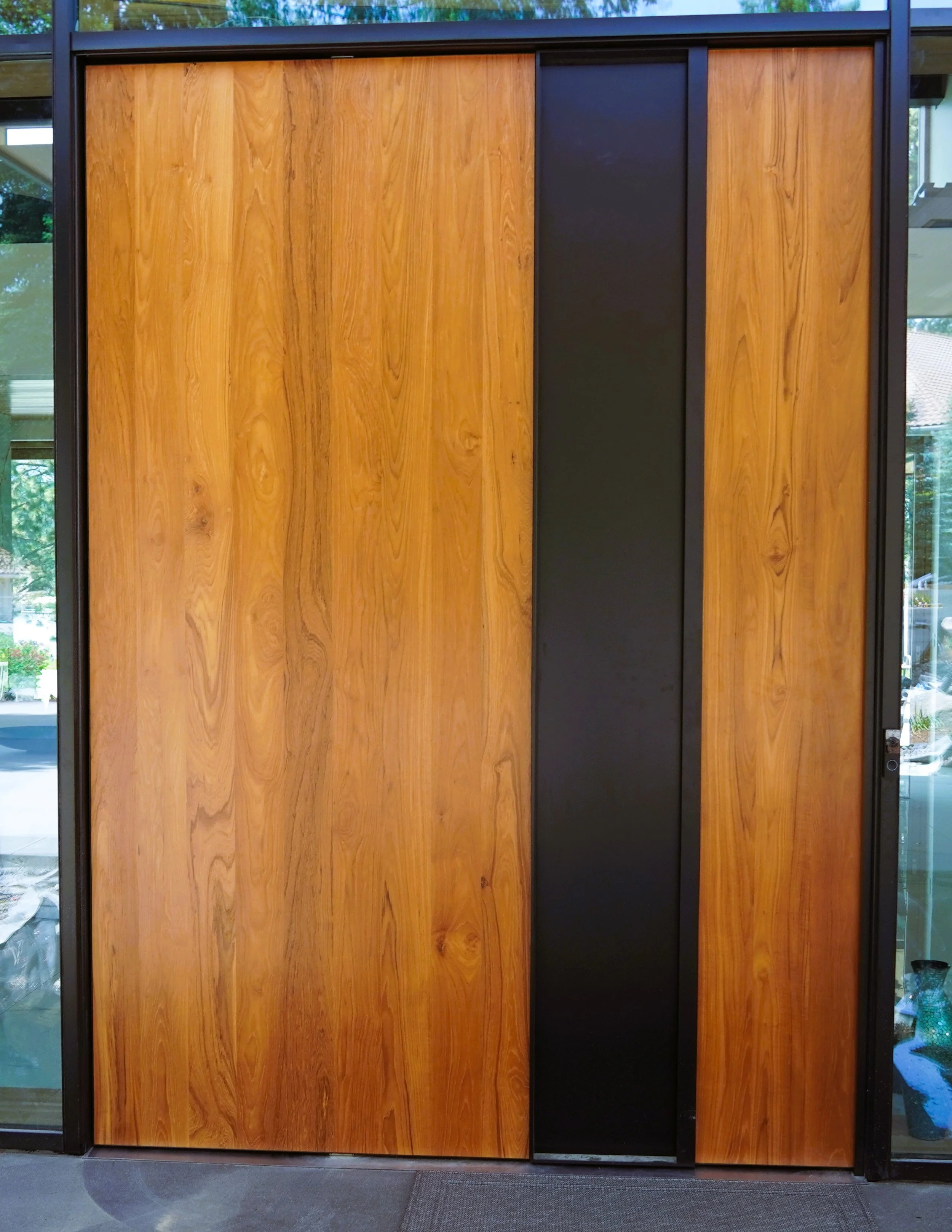 A wooden sliding door with a black vertical handle in the center, framed by black metal.