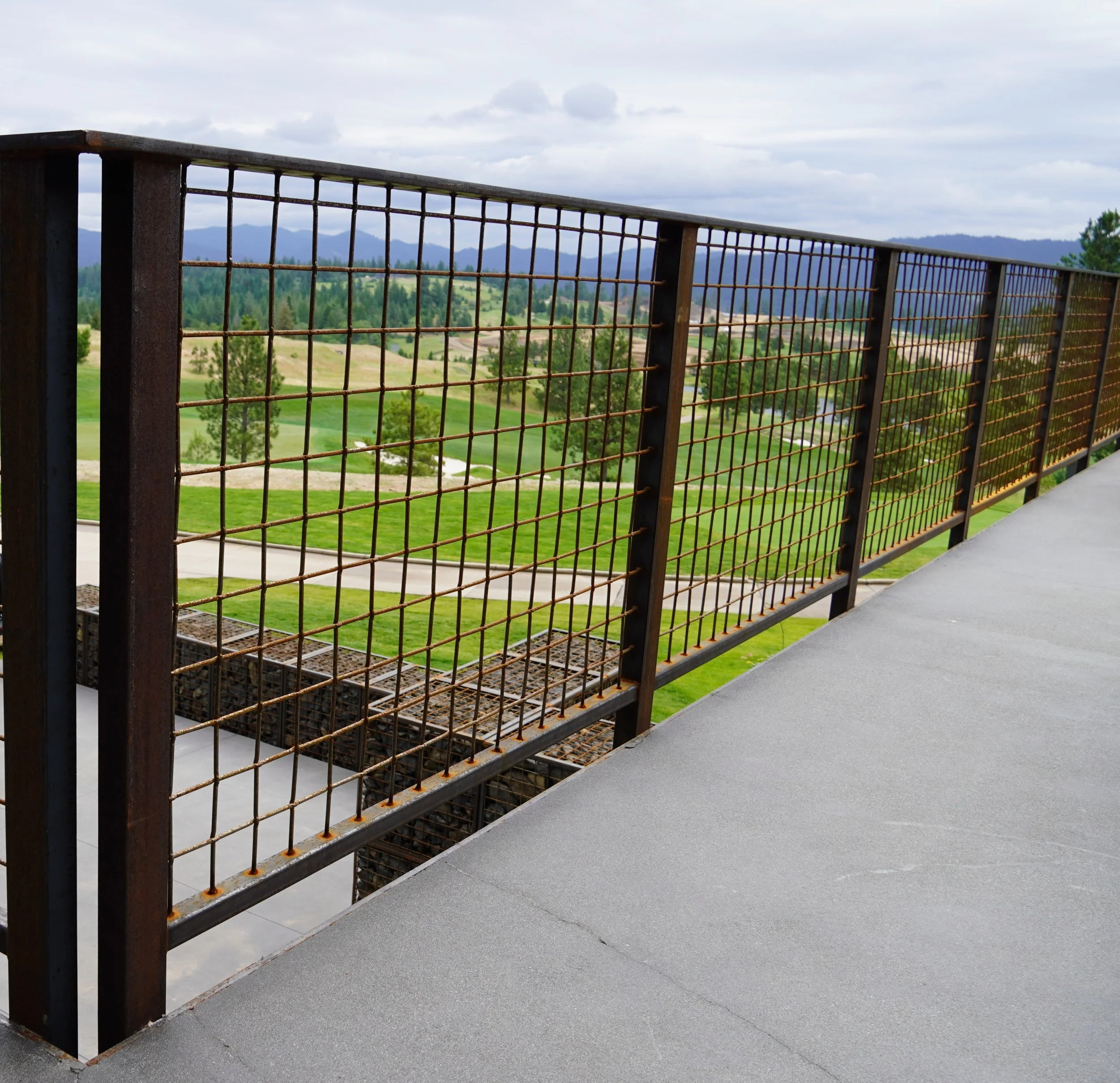 View from a balcony with a rusted metal safety railing overlooking a golf course with green grass, trees, and distant mountains.