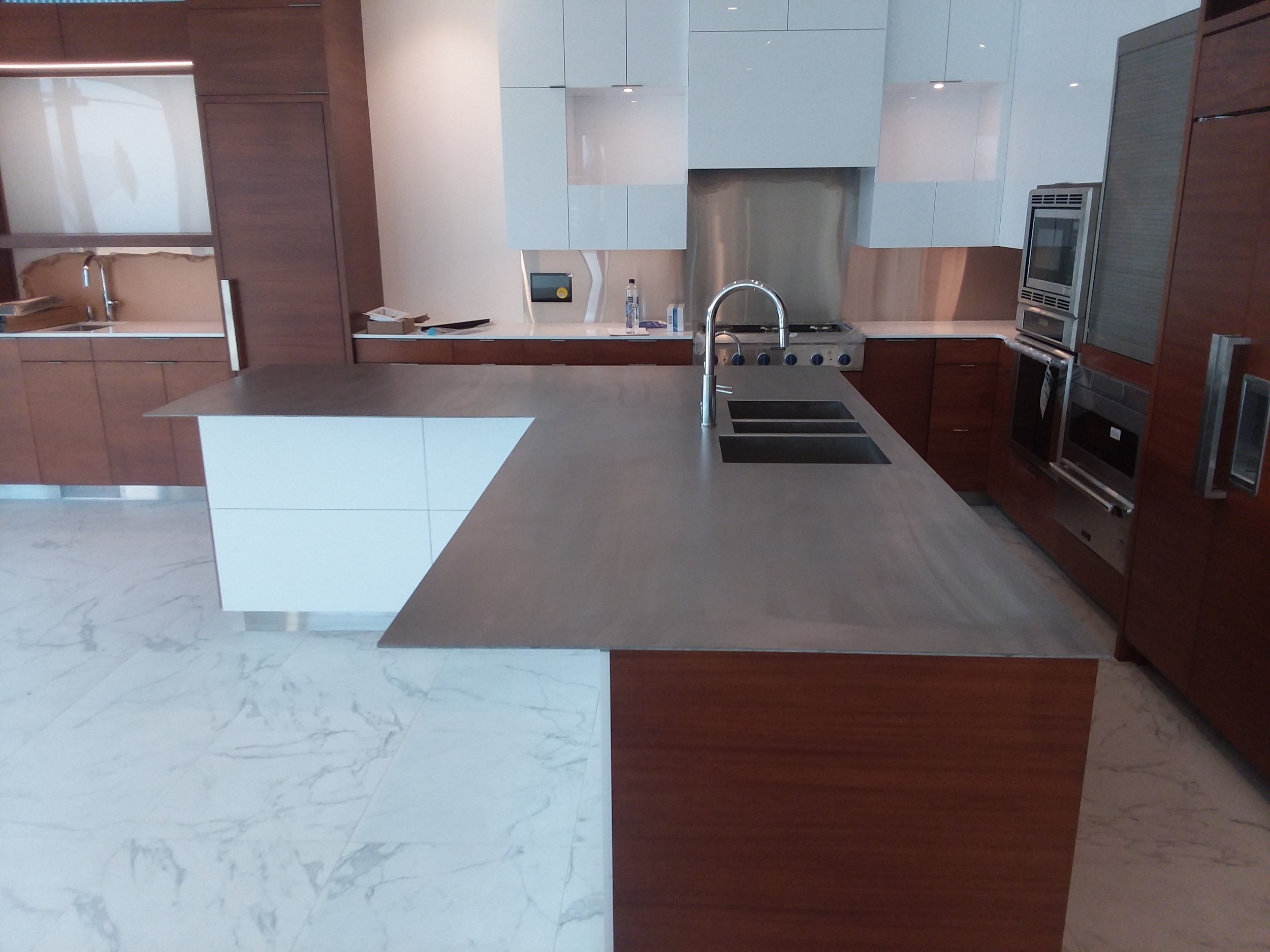Modern kitchen with dark wood cabinetry, stainless steel appliances, quartz countertops, and marble flooring.