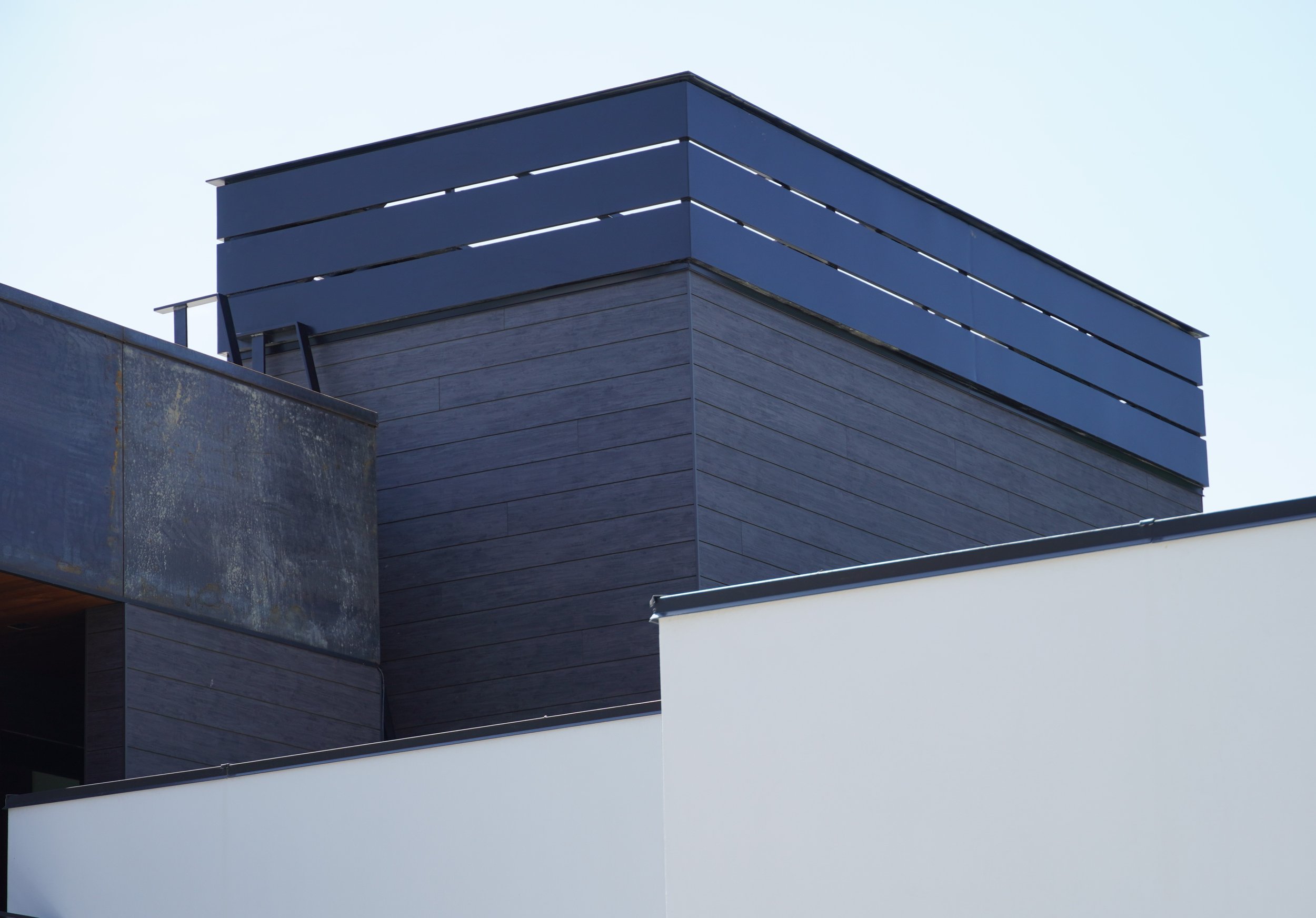Close-up of modern building with black wood siding and a white wall.