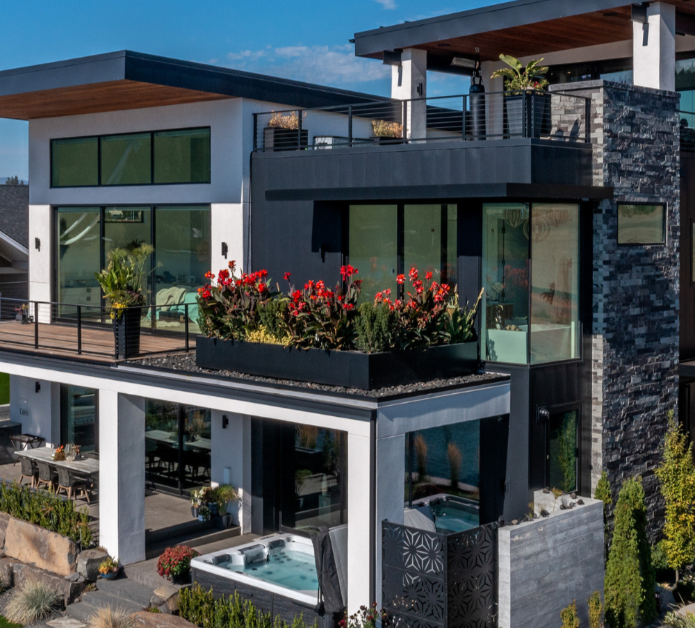 Modern multi-story house with large windows, outdoor patio, landscaped garden, and hot tub.