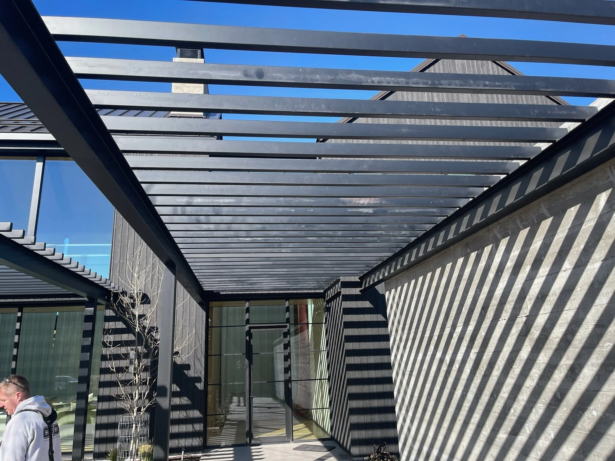 Modern building entrance with shadow-patterned awning, glass door, and a person standing outside.