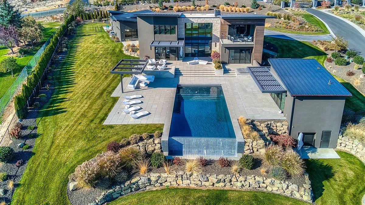 A modern house with a large outdoor patio, swimming pool, and landscaped yard seen from above.