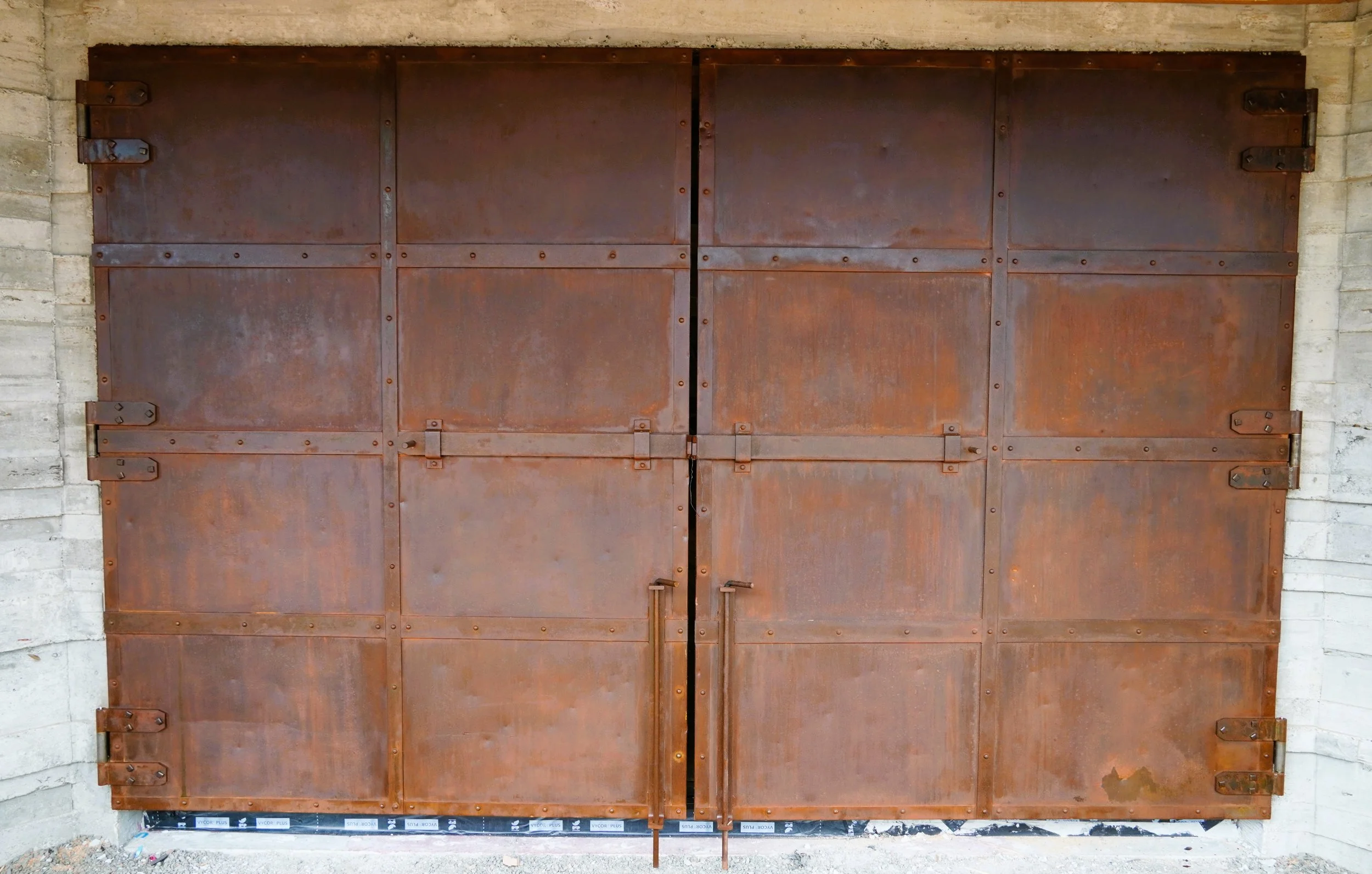 Large rusted metal garage door with hinges and handles, set in a concrete wall.