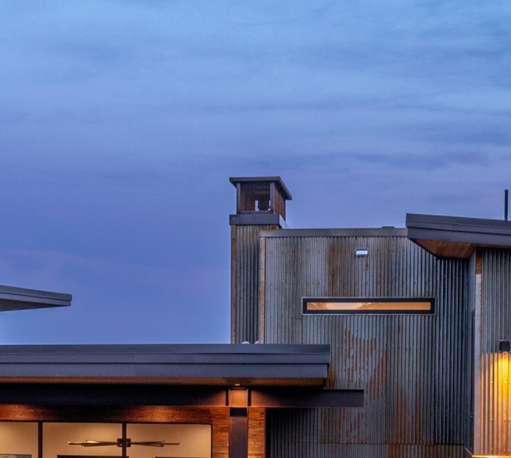 Exterior of a modern building with wooden siding and a small tower, under a cloudy evening sky.
