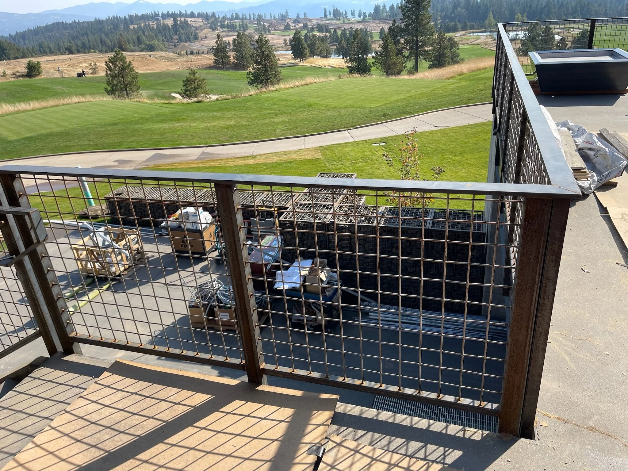 View from a balcony showing construction supplies and equipment below, with a scenic golf course and rolling hills in the background.