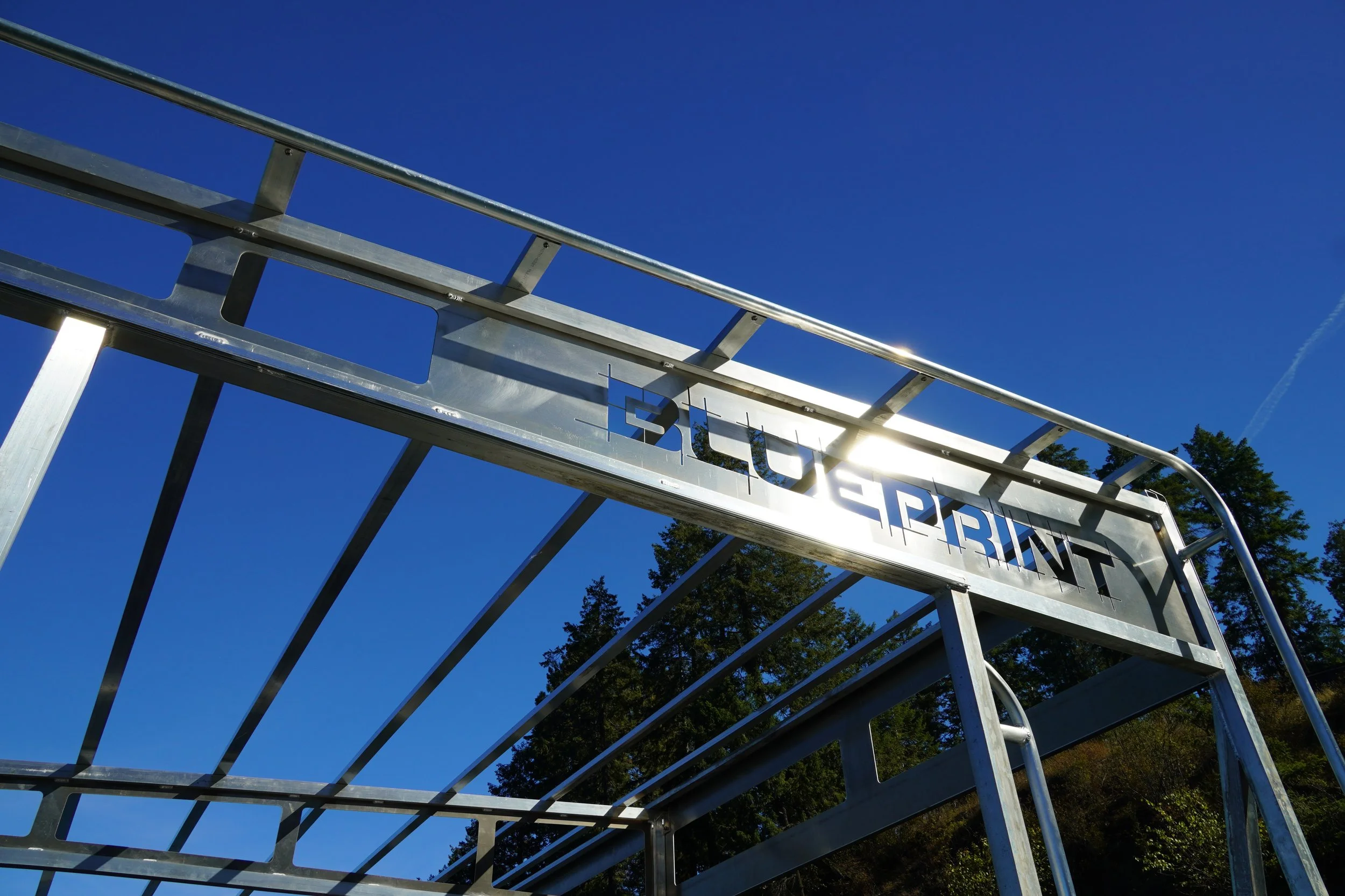 Metal framework of a building under construction against a clear blue sky, with trees in the background.