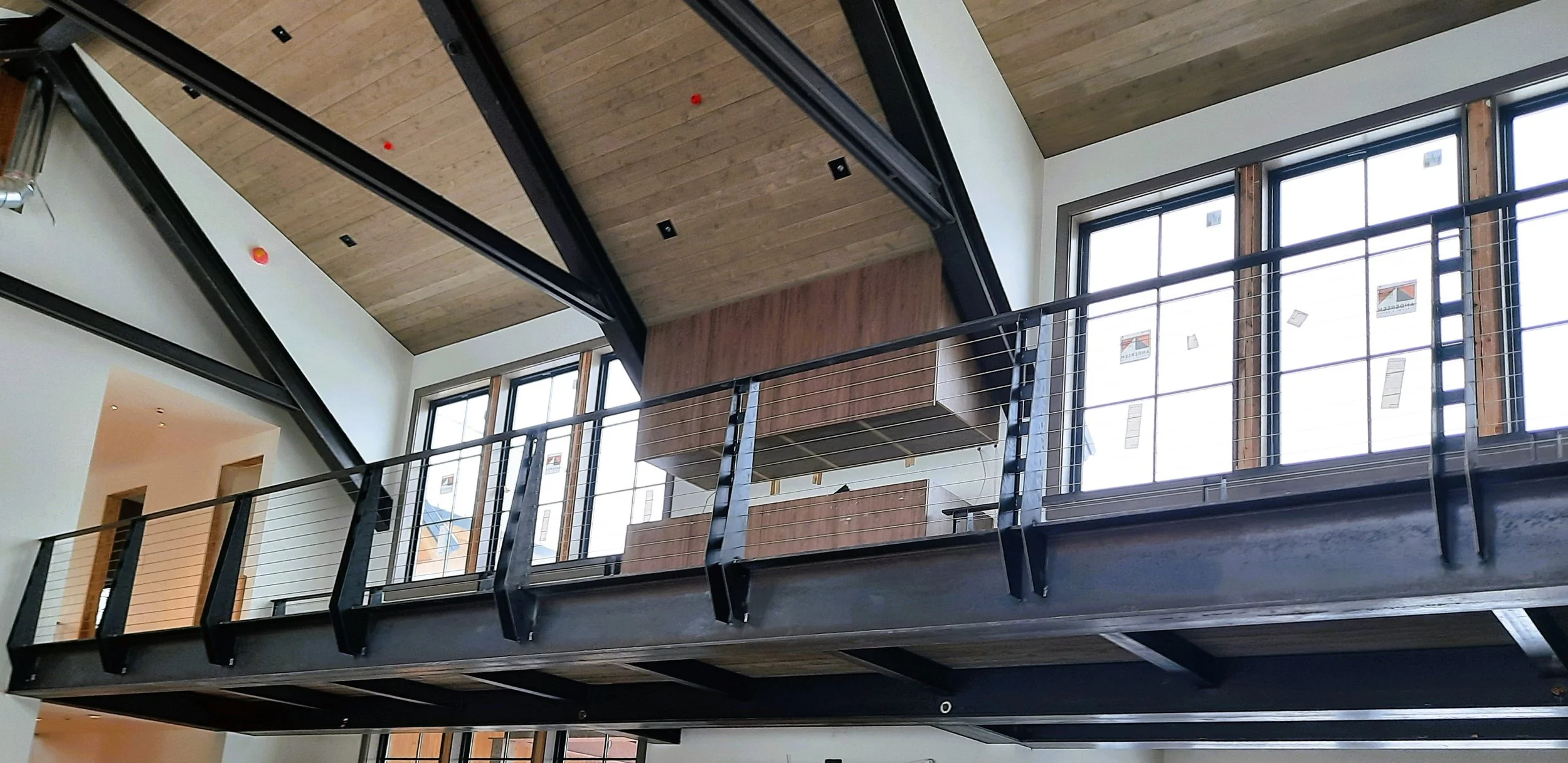 Interior of a modern building with a metal and cable balcony, large windows, and wood accents on the ceiling and walls.
