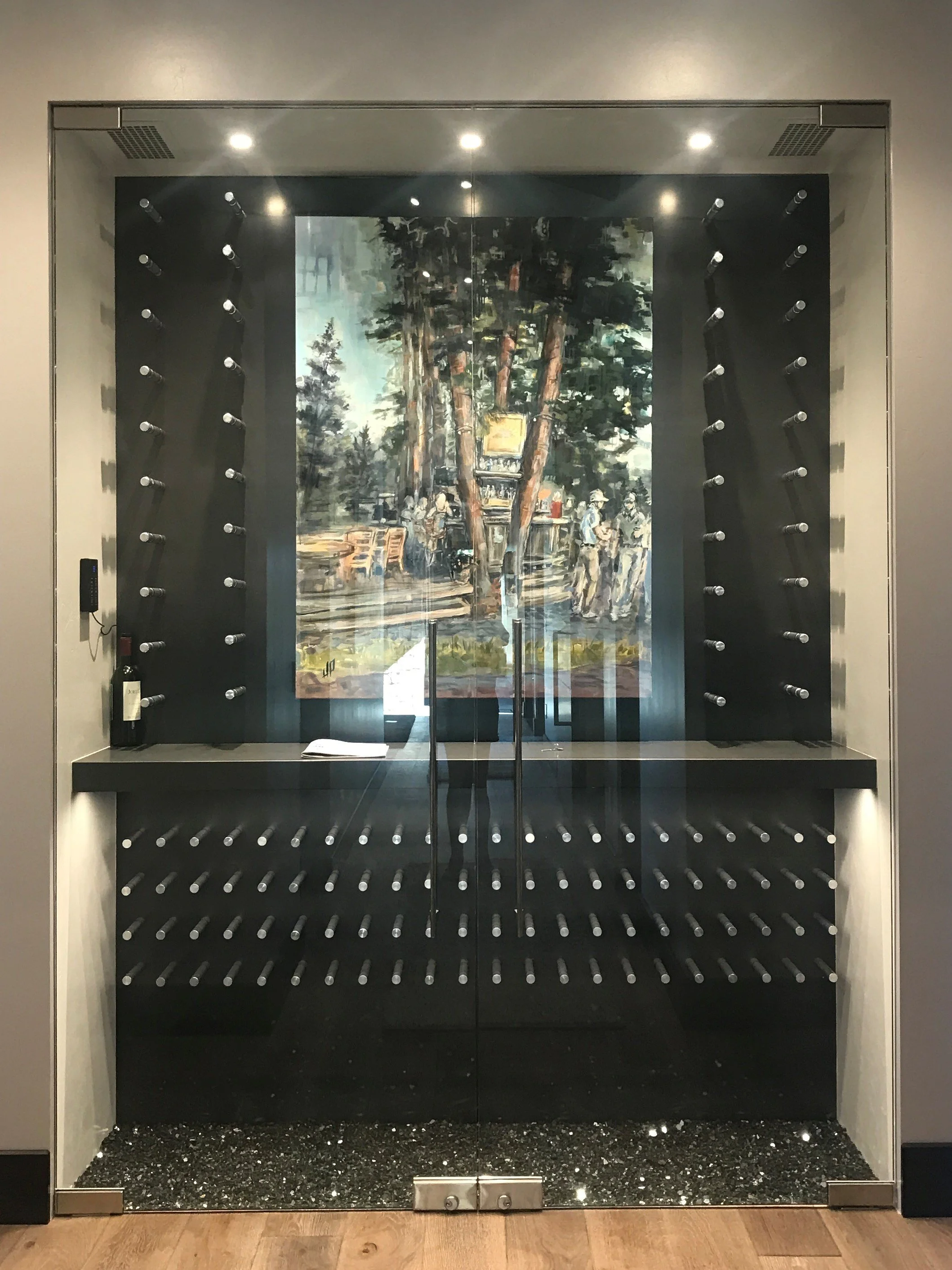 Glass display case with a painting of a park scene and several bottles of wine.