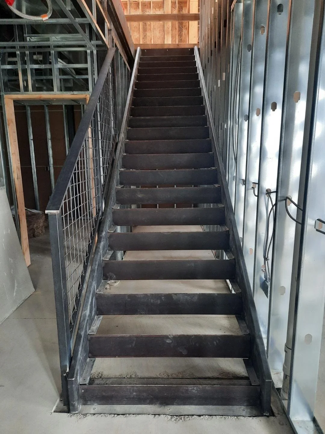 Metal staircase under construction in a building with exposed metal studs, electrical wiring, and framing.