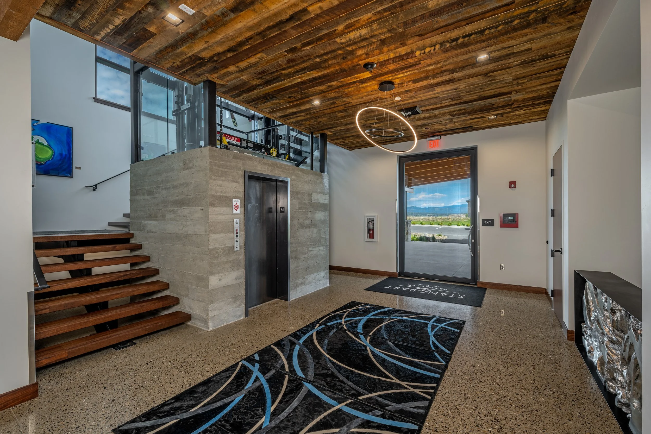 Modern lobby with a wooden ceiling, elevator, stairs, and large glass door