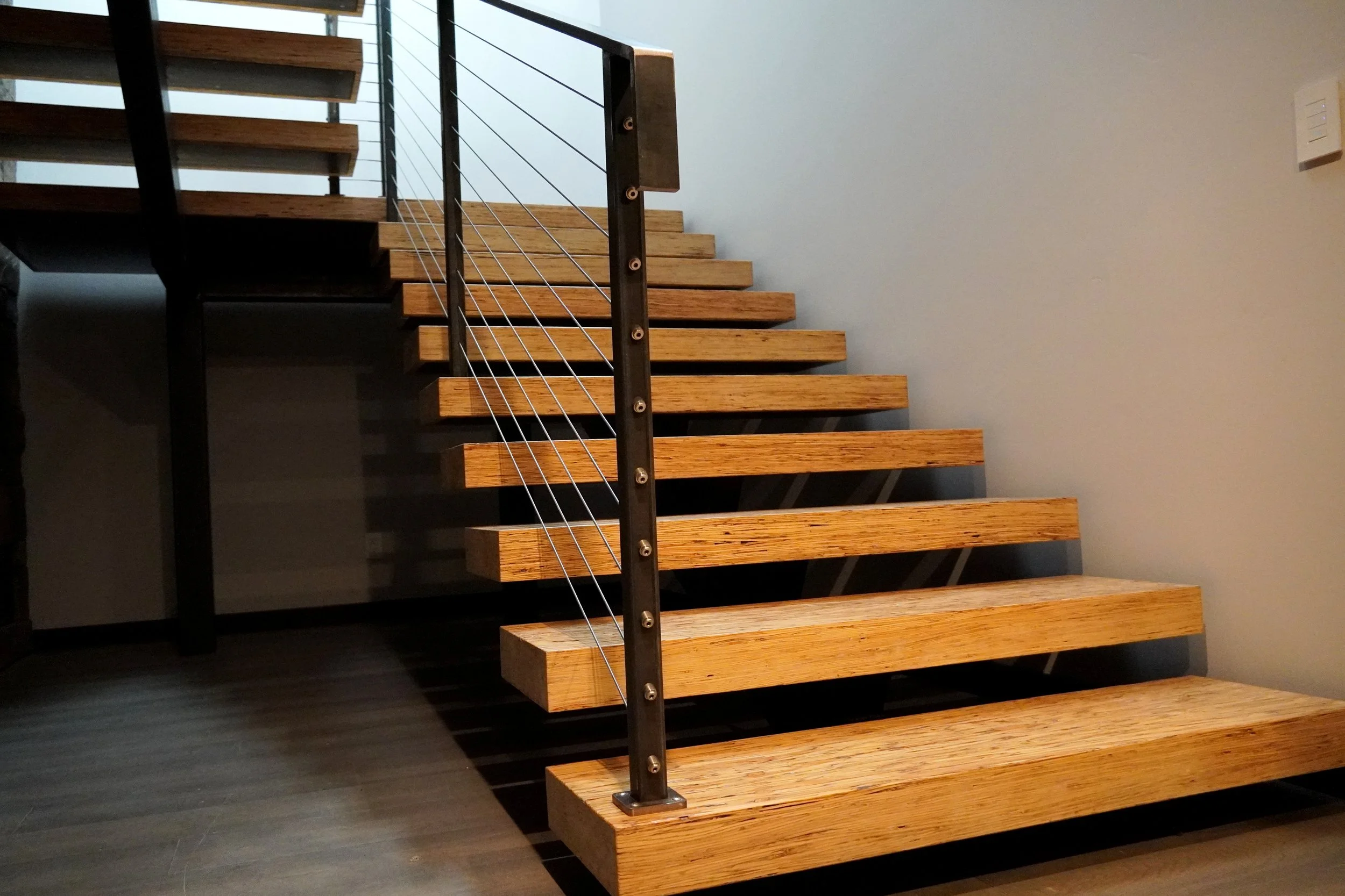 Wooden staircase with metal railing and cable balusters inside a modern home.