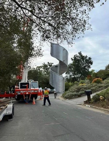 A construction site on a street with a large metal spiral slide and workers in safety gear.